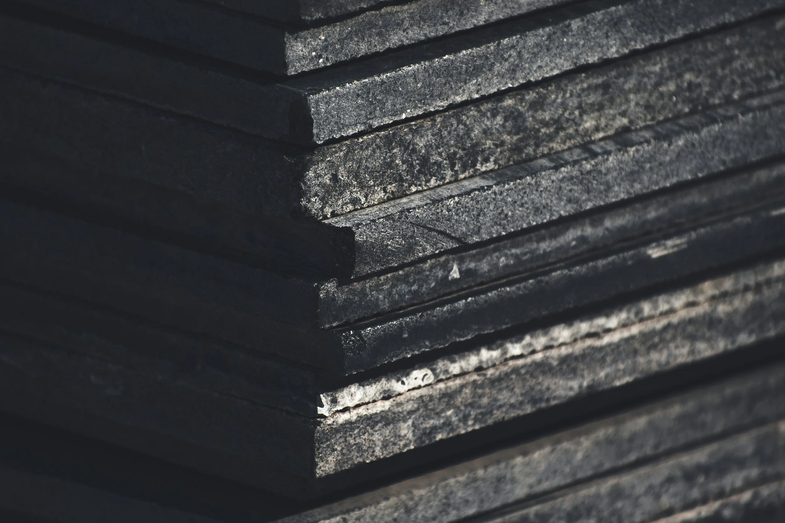 Close-up of stacked dark gray rectangular stones or tiles with rough texture, arranged neatly.