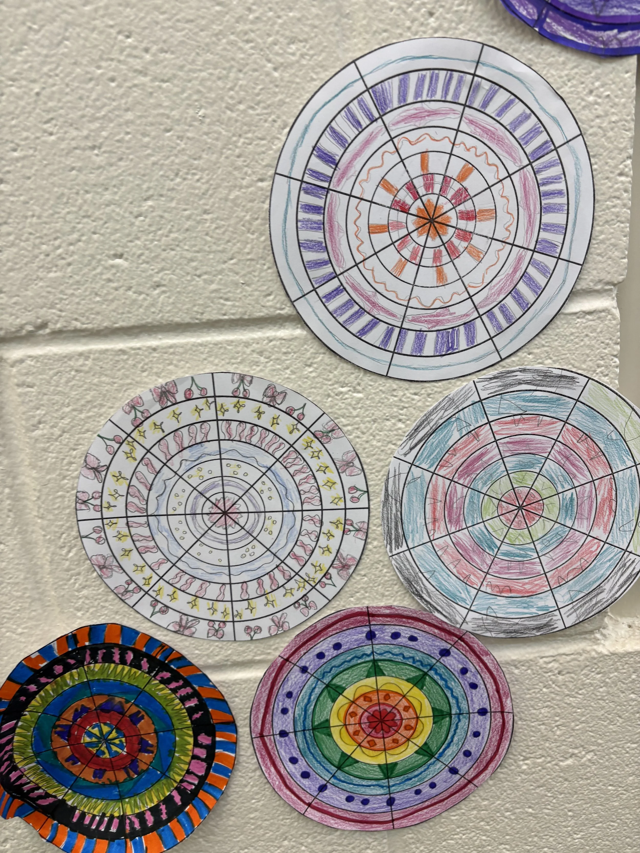 Five colorful circular drawings with various patterns, mounted on a beige wall.