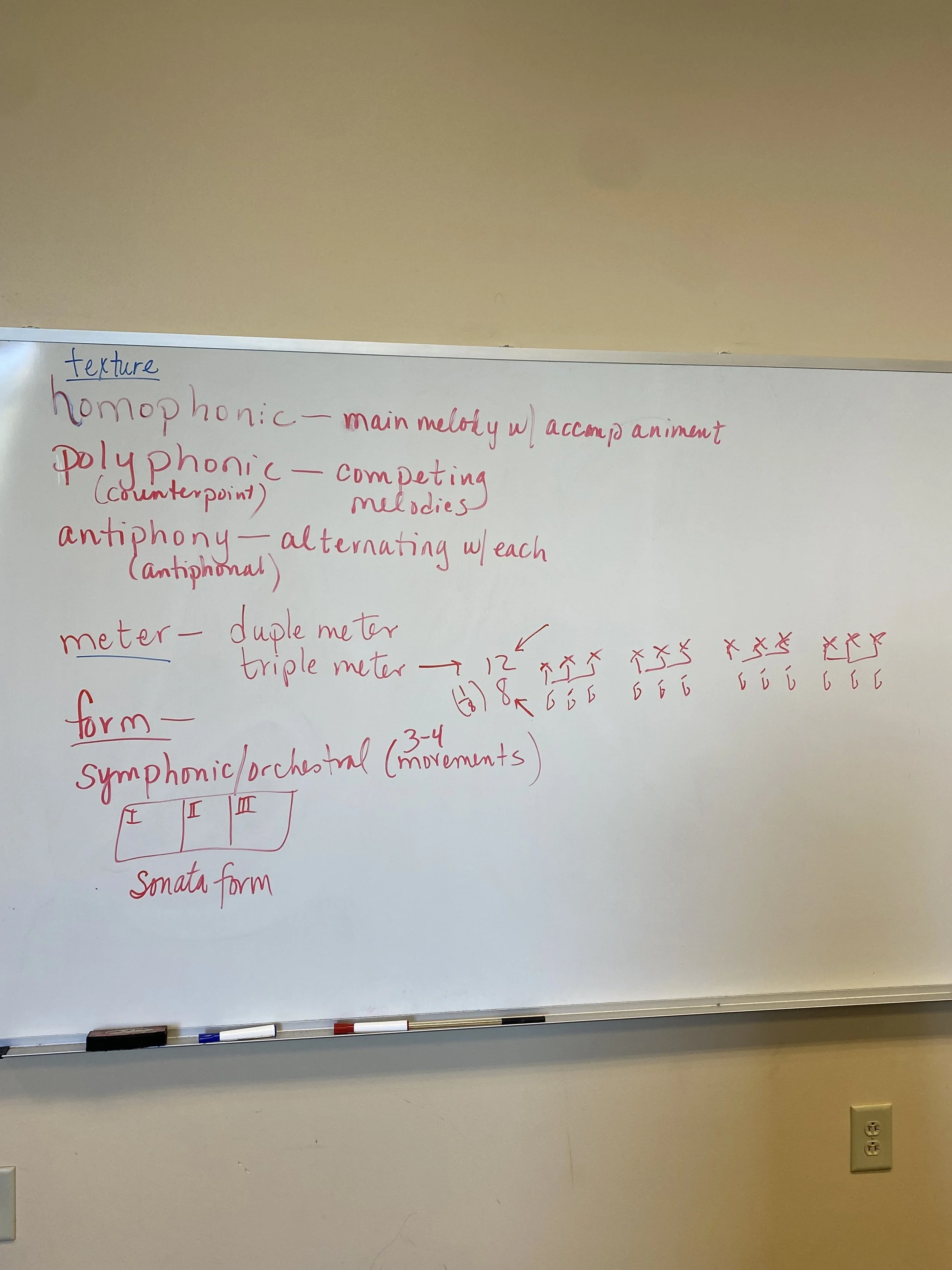 Whiteboard with handwritten music theory notes, including definitions of homophonic, polyphonic, and antiphony, diagrams of meter and form, and mentions of symphonic/orchestral and sonata form.
