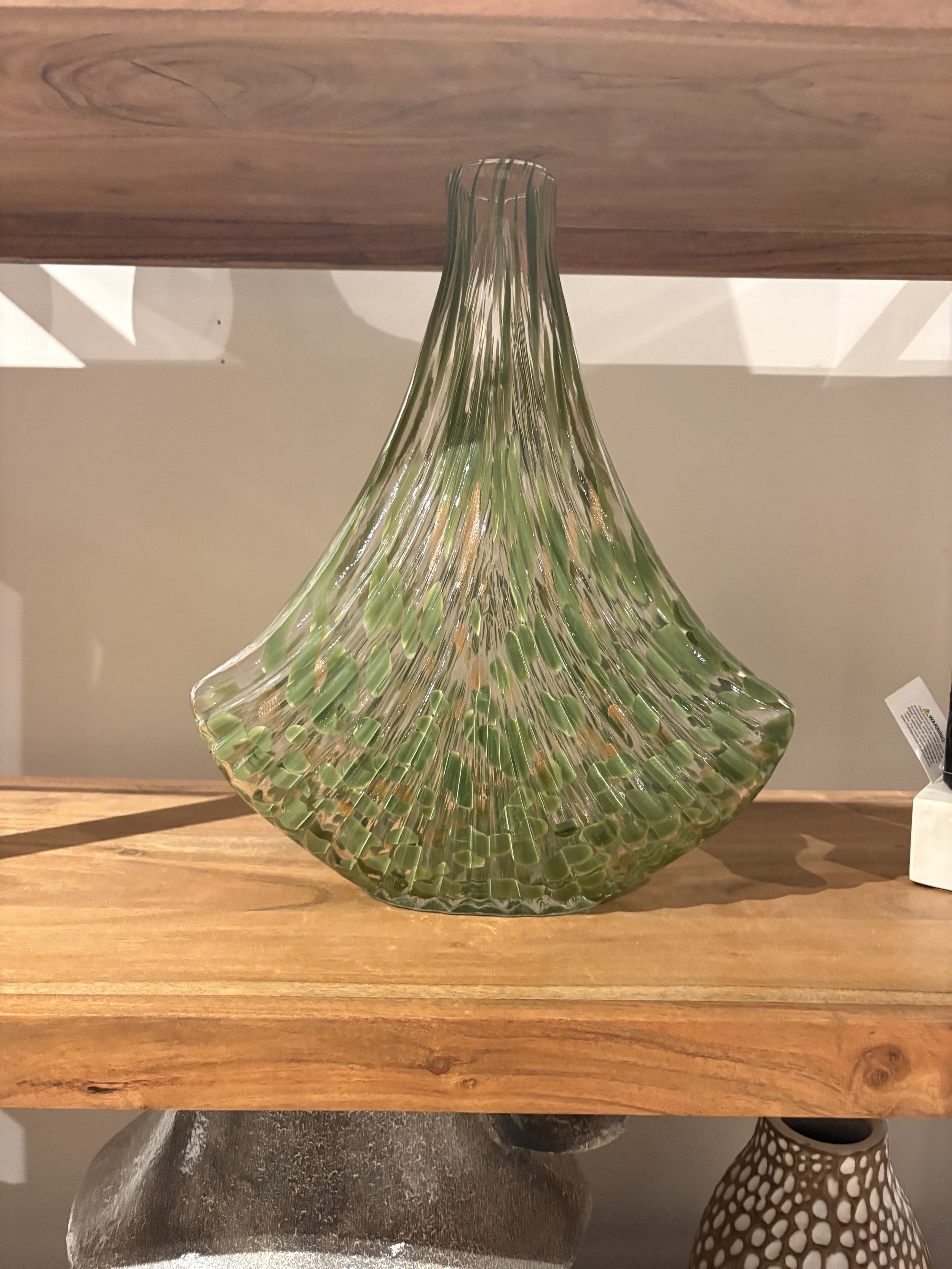 Green and clear art glass vase with vertical ridges on a wooden shelf.