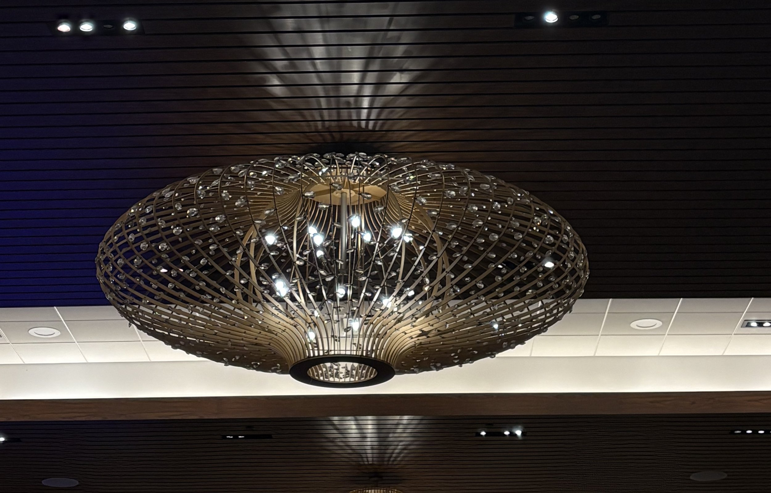 A modern chandelier with multiple small lights, encased in a decorative wooden lattice, casting intricate shadows on the ceiling.