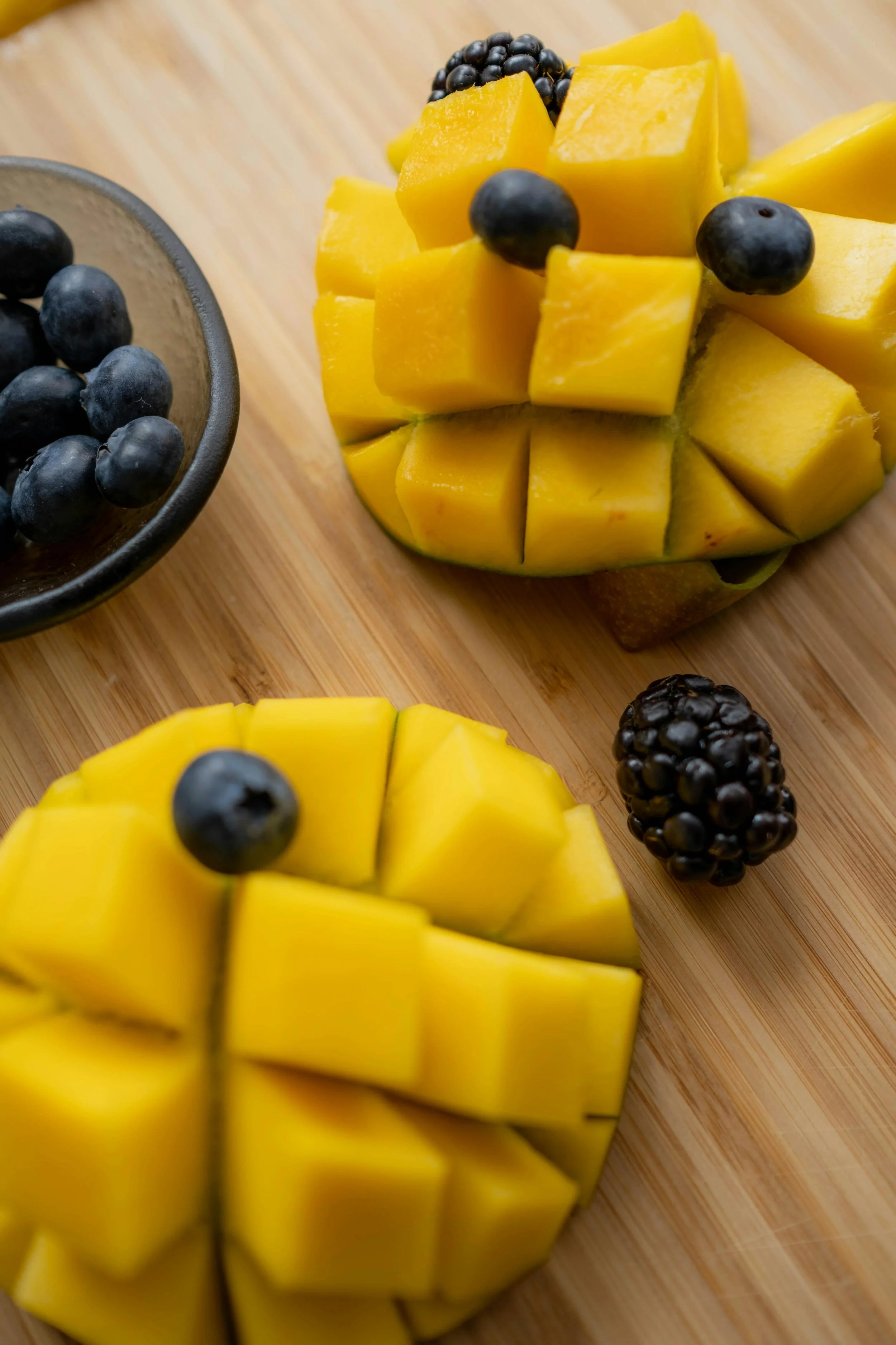 Sliced mango with blueberries on a wooden cutting board, with a small glass bowl of blueberries.