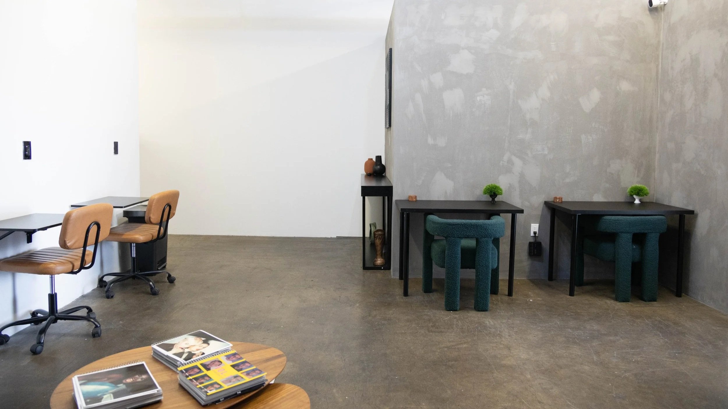 Modern office or lounge with a white wall, gray concrete-textured wall, desks, chairs, and decorative vases and plants. This is MuseWorks Studio in Downtown Arts District in Los Angeles.