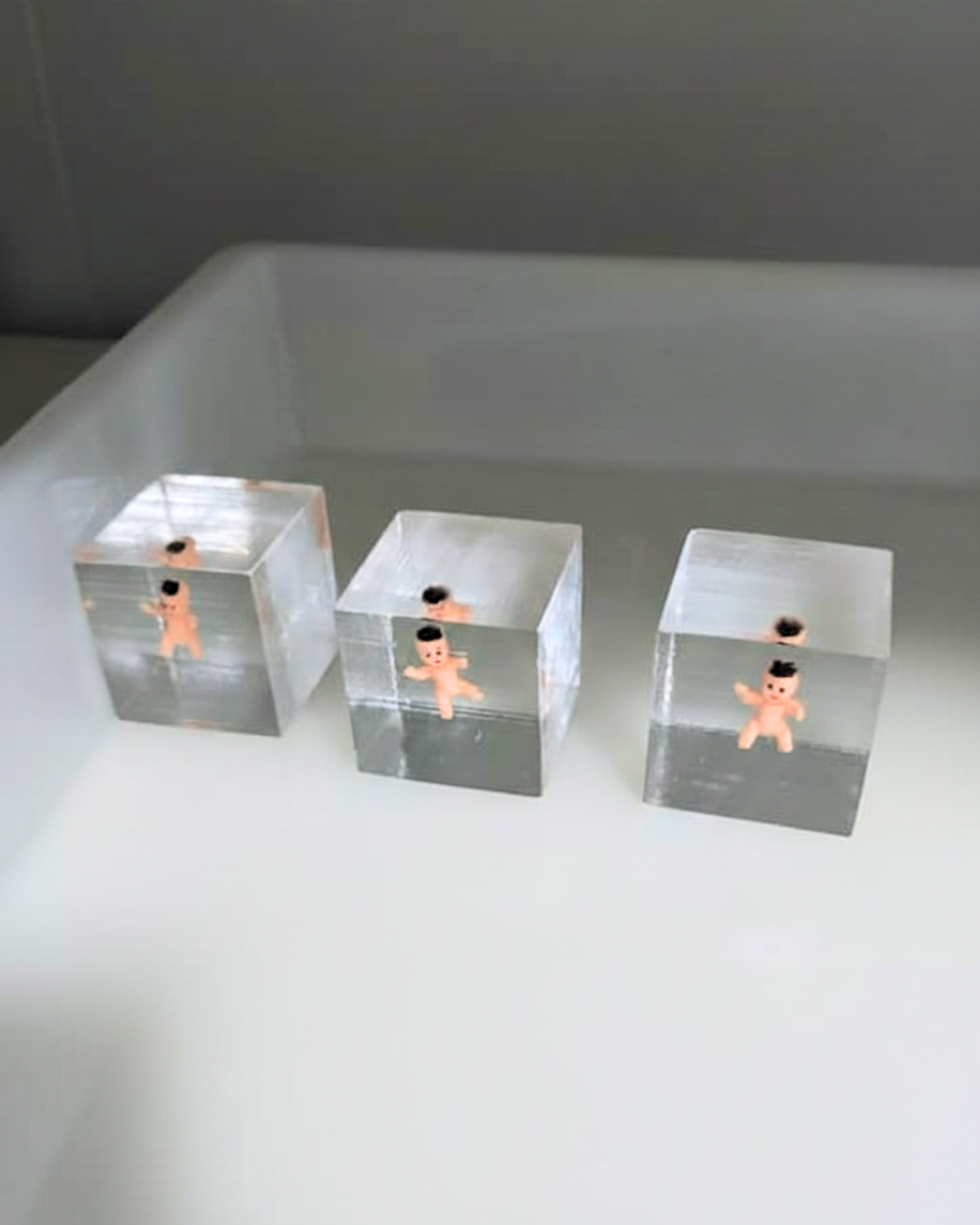 Three transparent acrylic blocks each containing a small plastic doll submerged in water