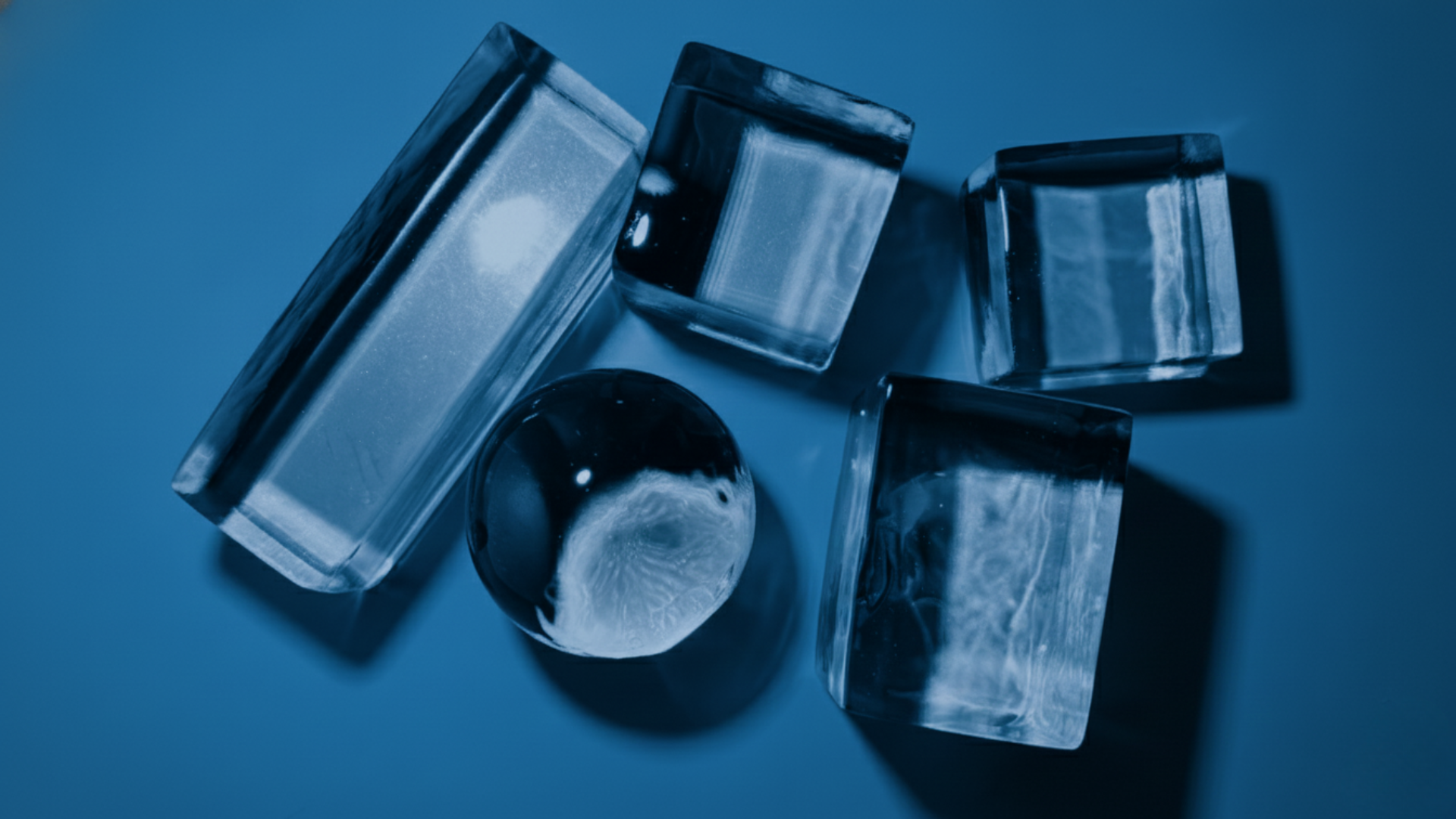 Six ice cubes and one ice sphere on a blue surface