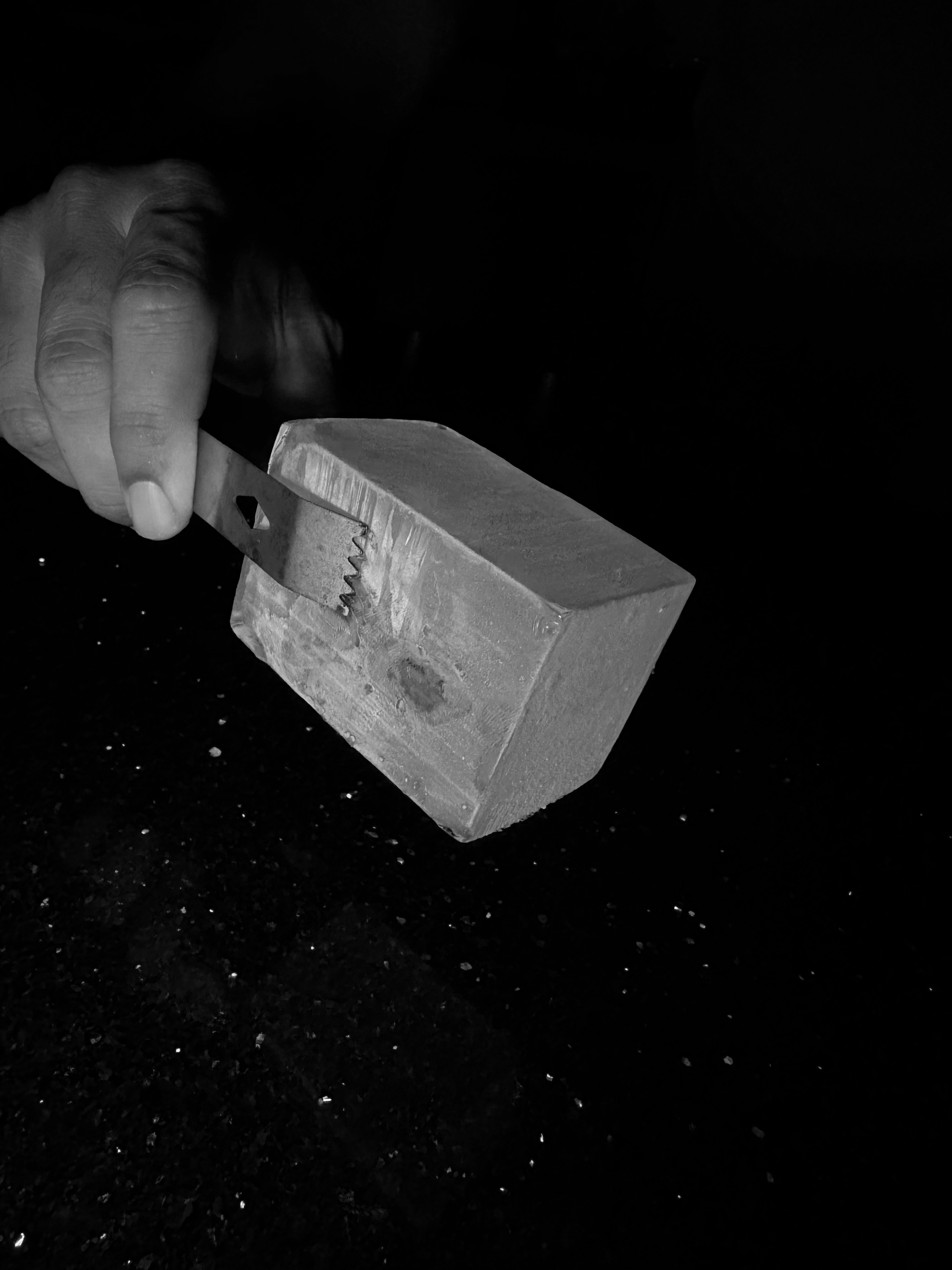 A person's hand holding a box cutter blade near a rectangular block.