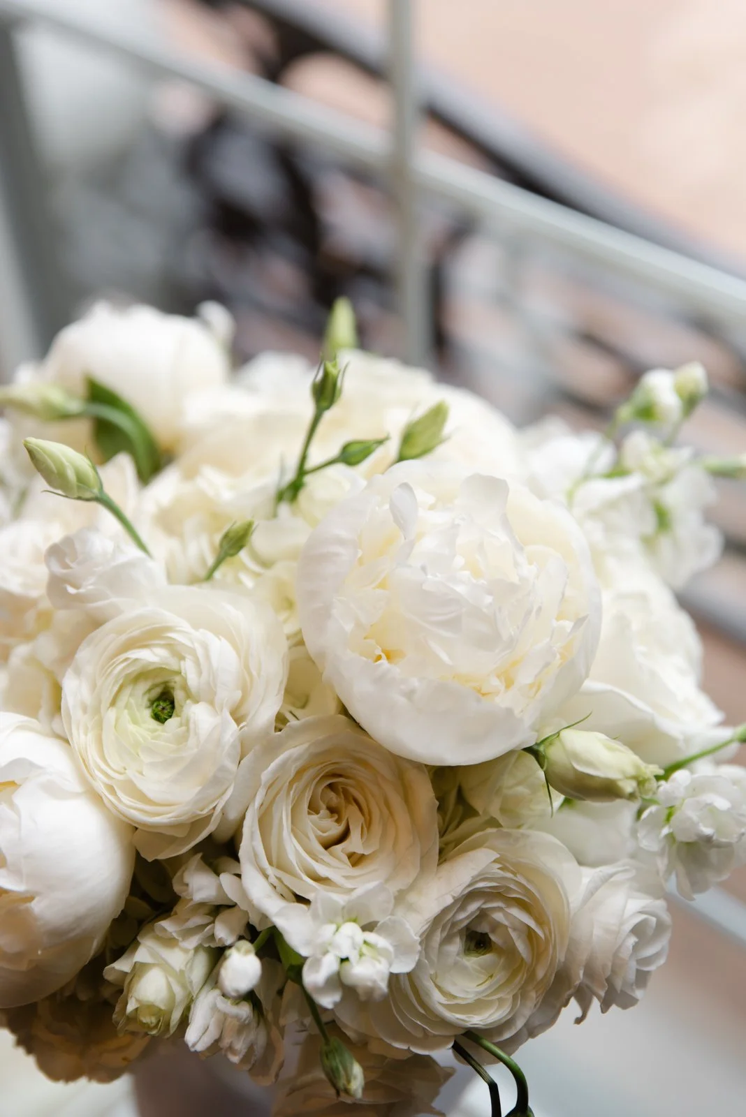 A bouquet of white flowers including roses and other blooms with green buds, set against a blurred background.