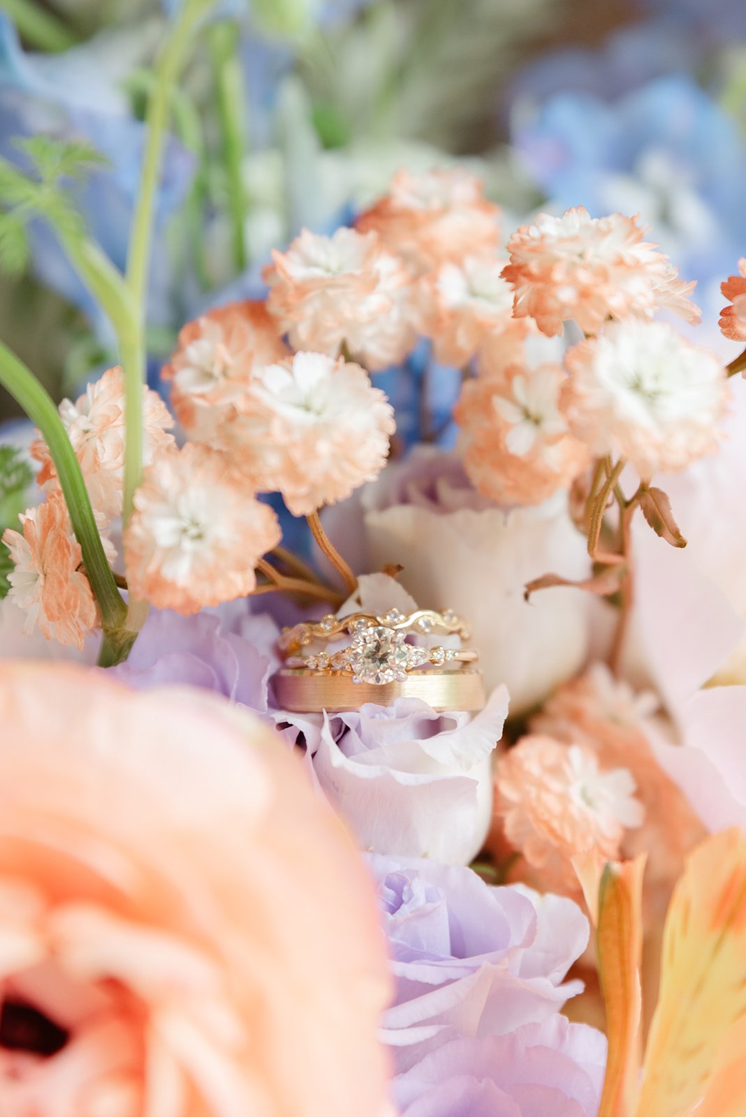 Wedding rings surrounded by peach and lavender flowers.