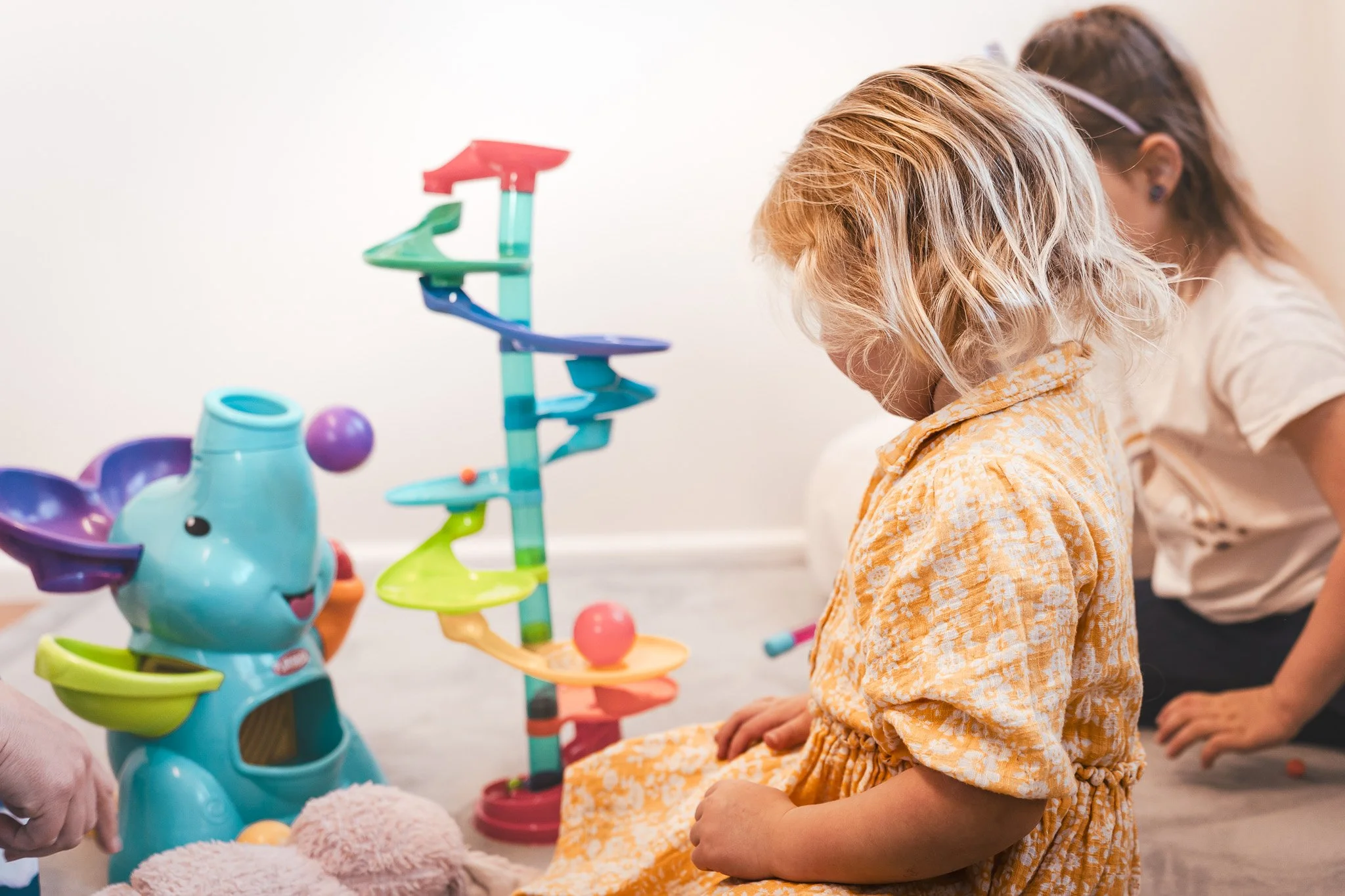Two children playing with a colorful marble run and an elephant-shaped toy on the floor indoors.