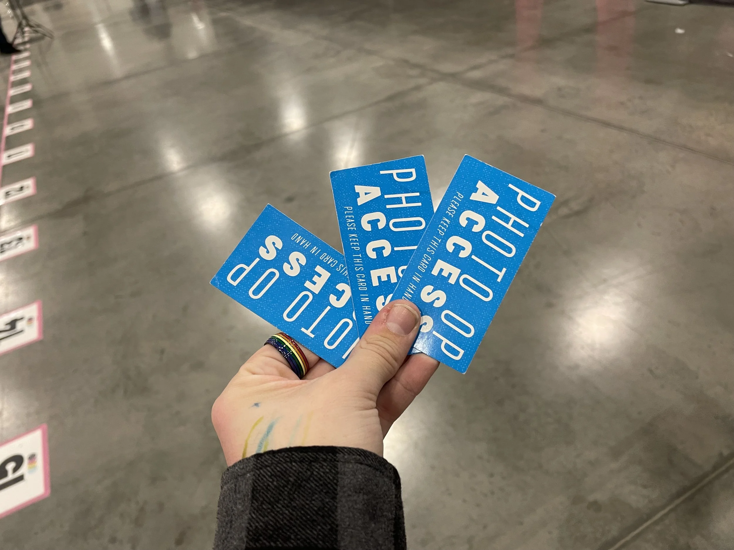 Hand holding three blue photo booth appointment tickets with white text that read 'PHOTO OP', 'ACCES,