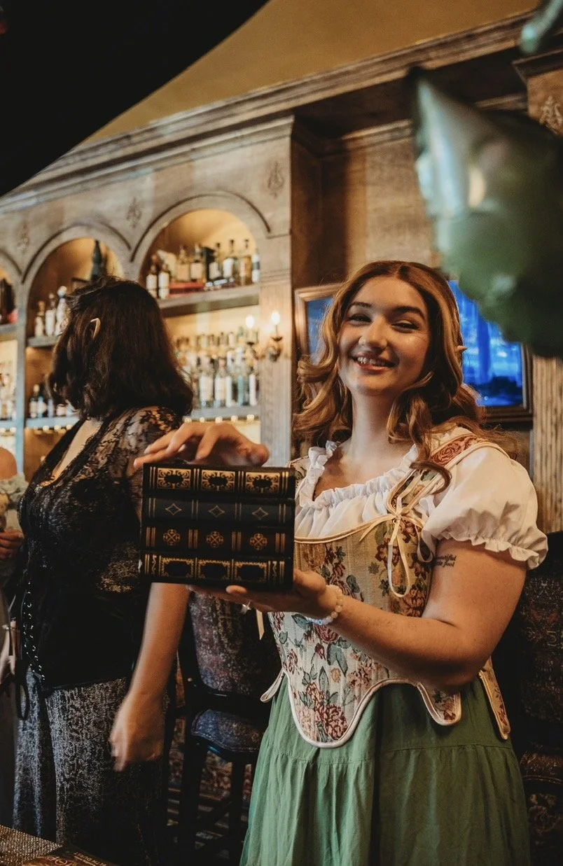 Young woman in traditional Bavarian dress holding a gift box and smiling at a bar or restaurant.