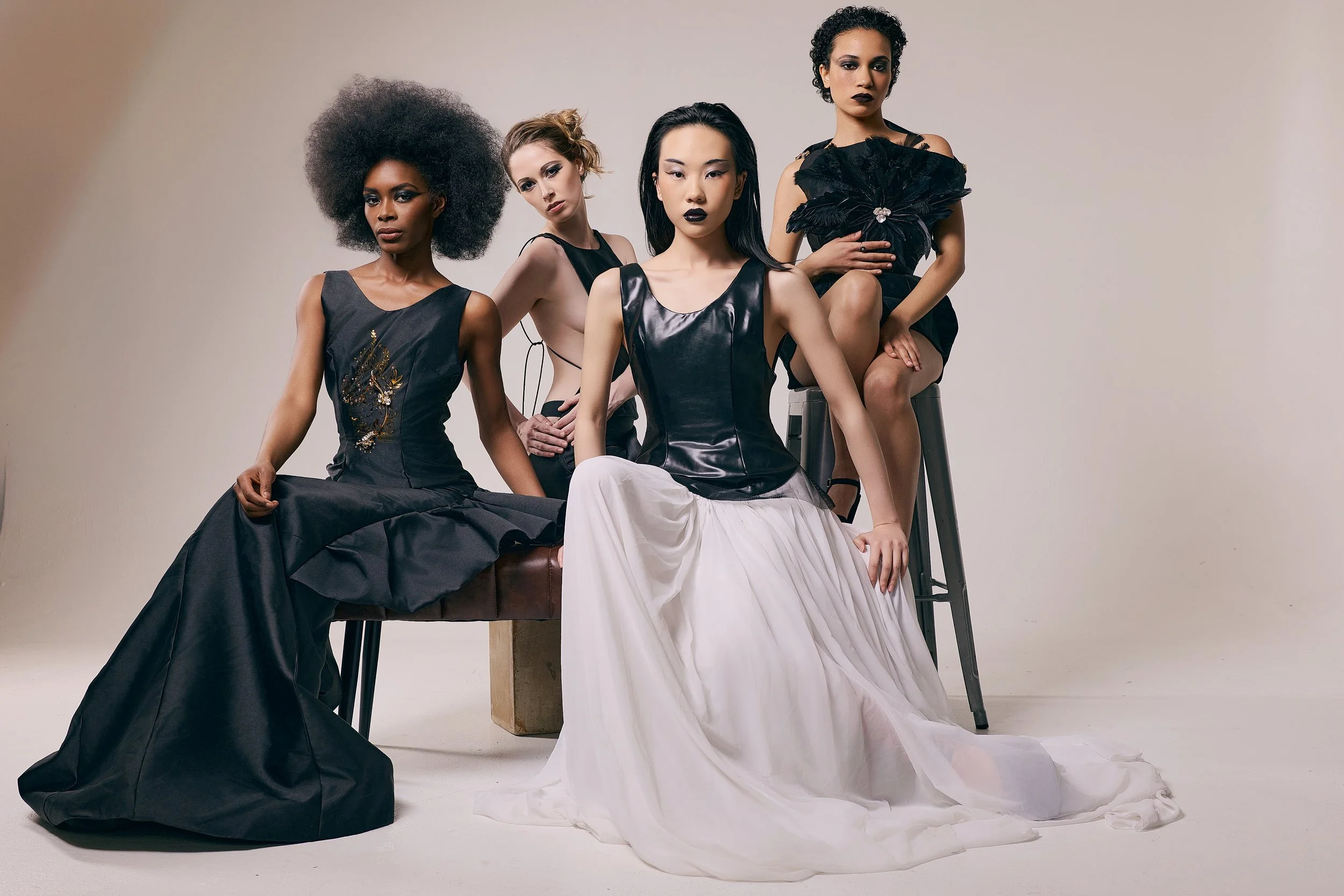 Four women wearing black and white formal dresses, sitting and standing against a plain background, with an emphasis on fashion and style.