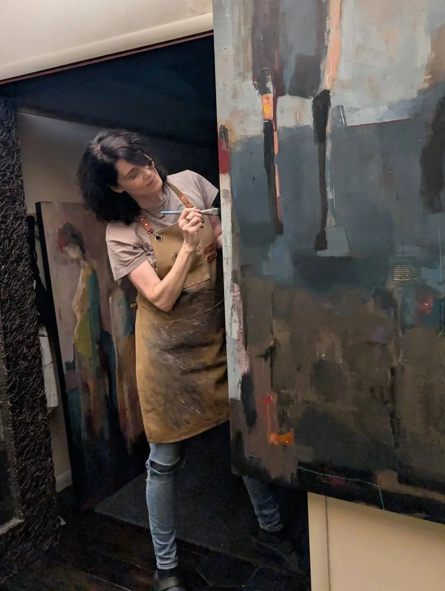 artist painting a large abstract figurative canvas in a studio with multiple works in progress
