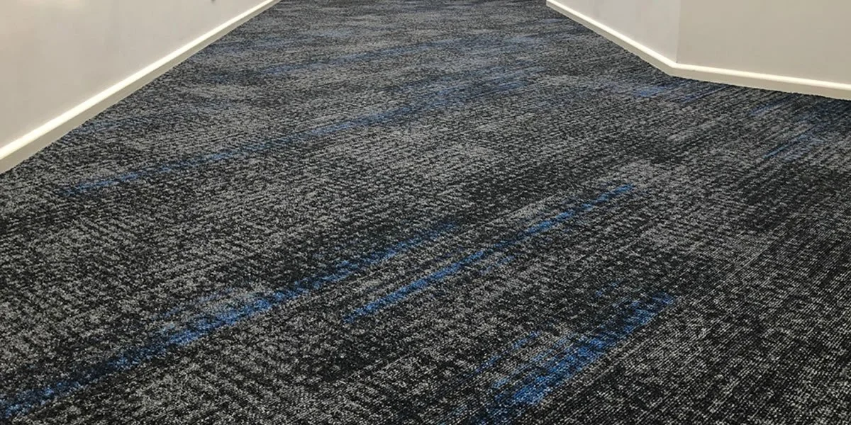 Close-up of a dark-colored, patterned carpet in an indoor setting with white walls and baseboards.