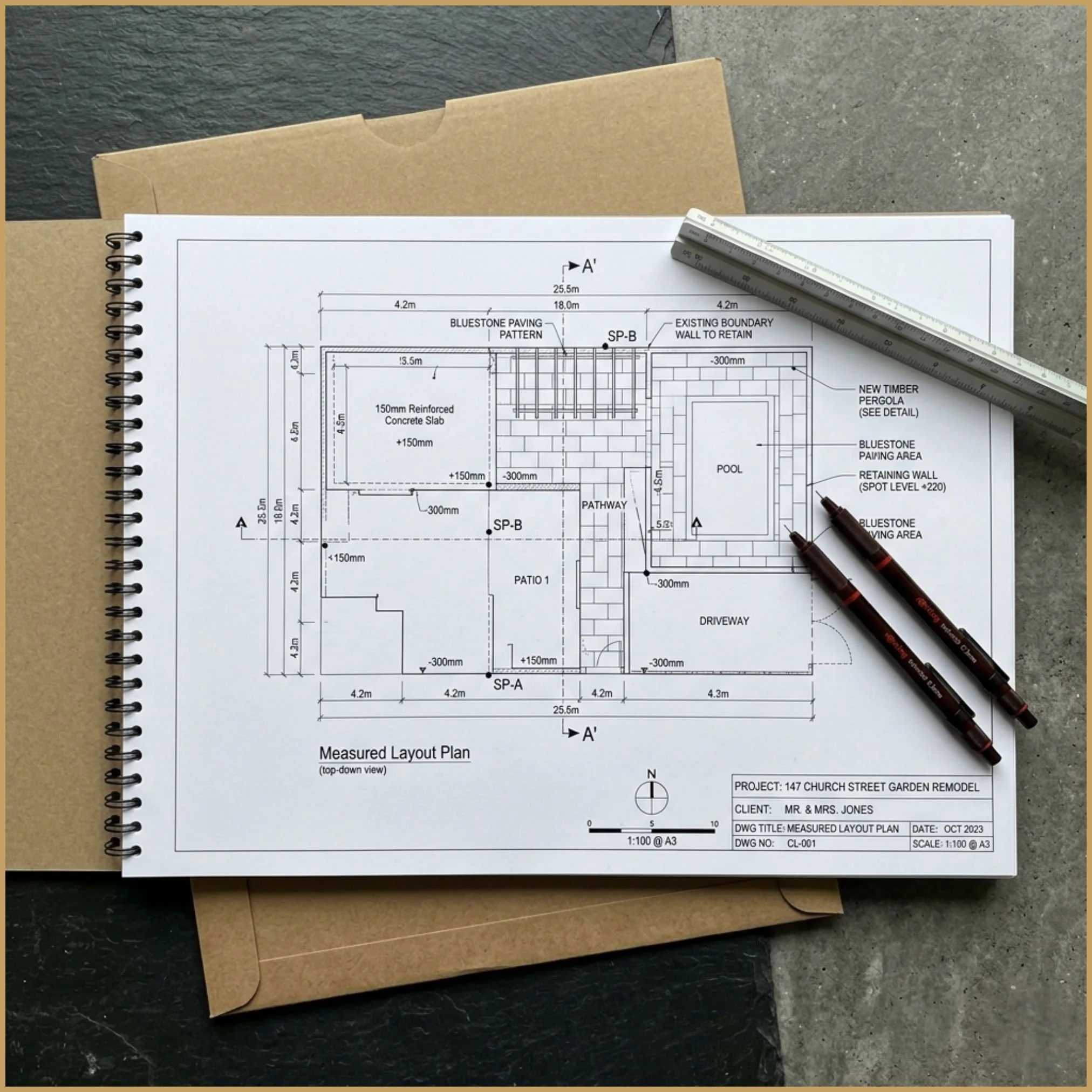 Flat-lay of an A3 printed contractor dossier with a rigid mailer. The open page displays a precise measured garden layout with clear dimensions.