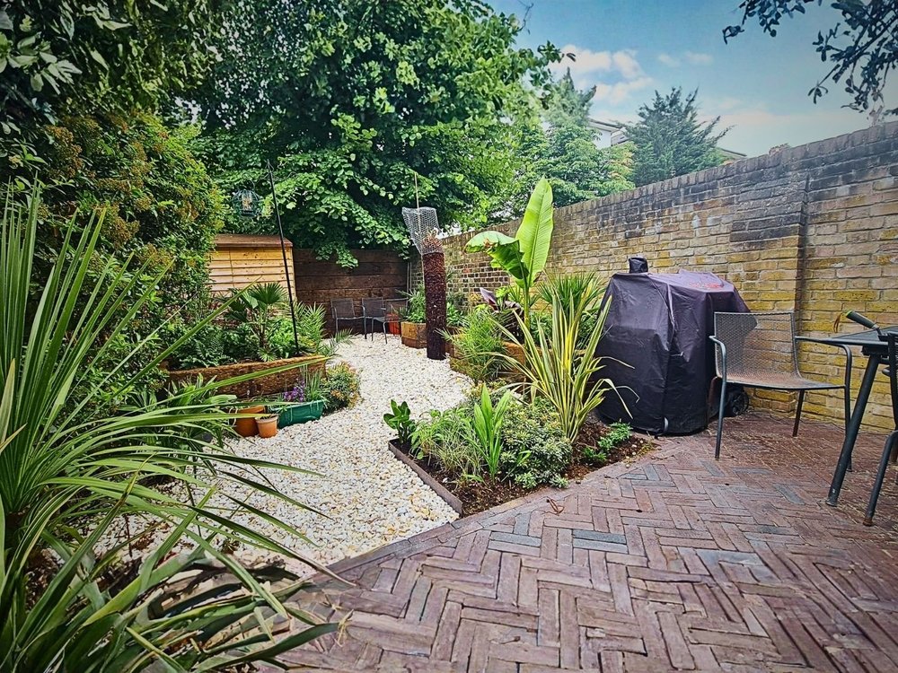 Completed small London garden with herringbone paving tropical planting and reclaimed sleeper raised beds