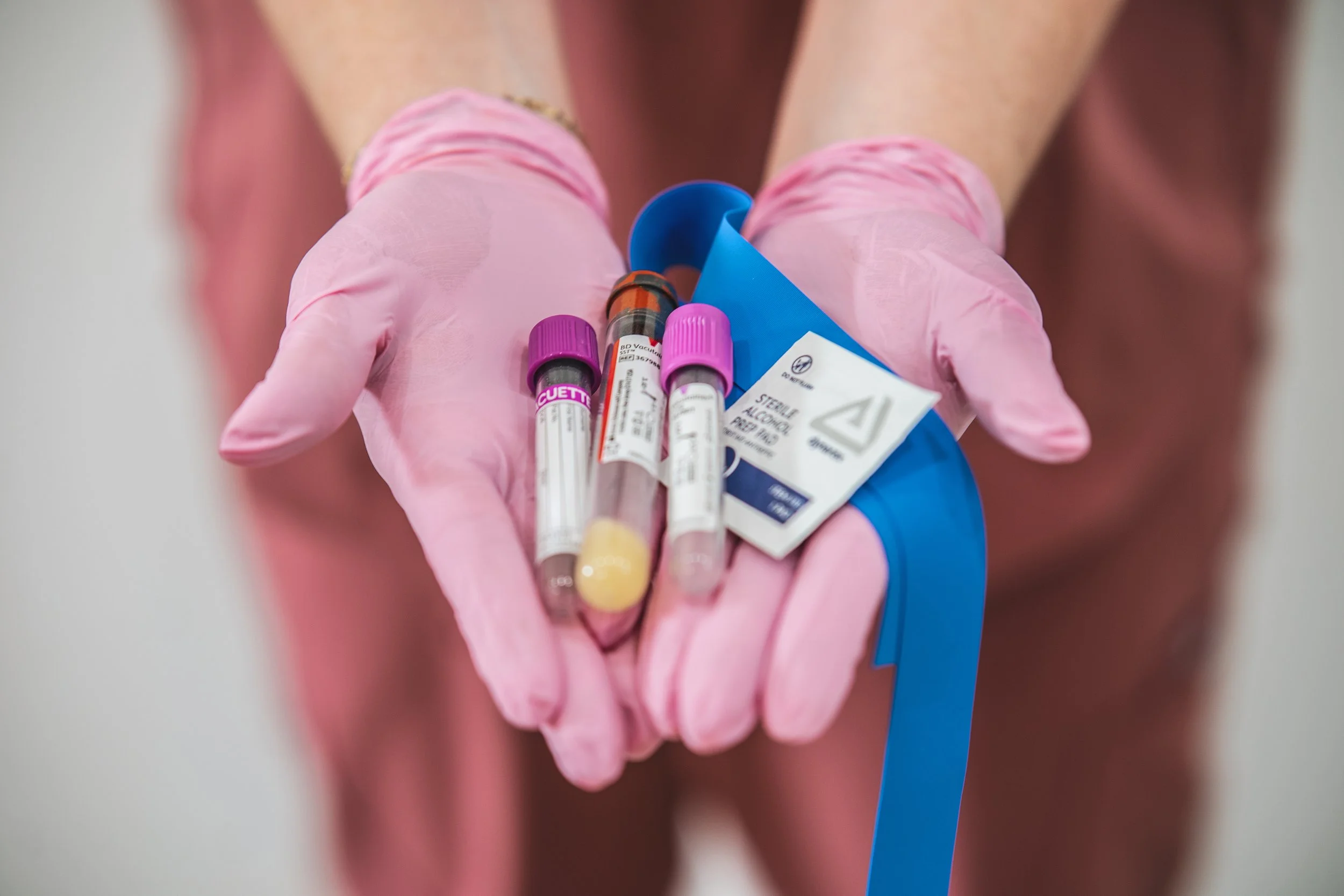 A person wearing pink gloves holding several test tubes with blood samples.