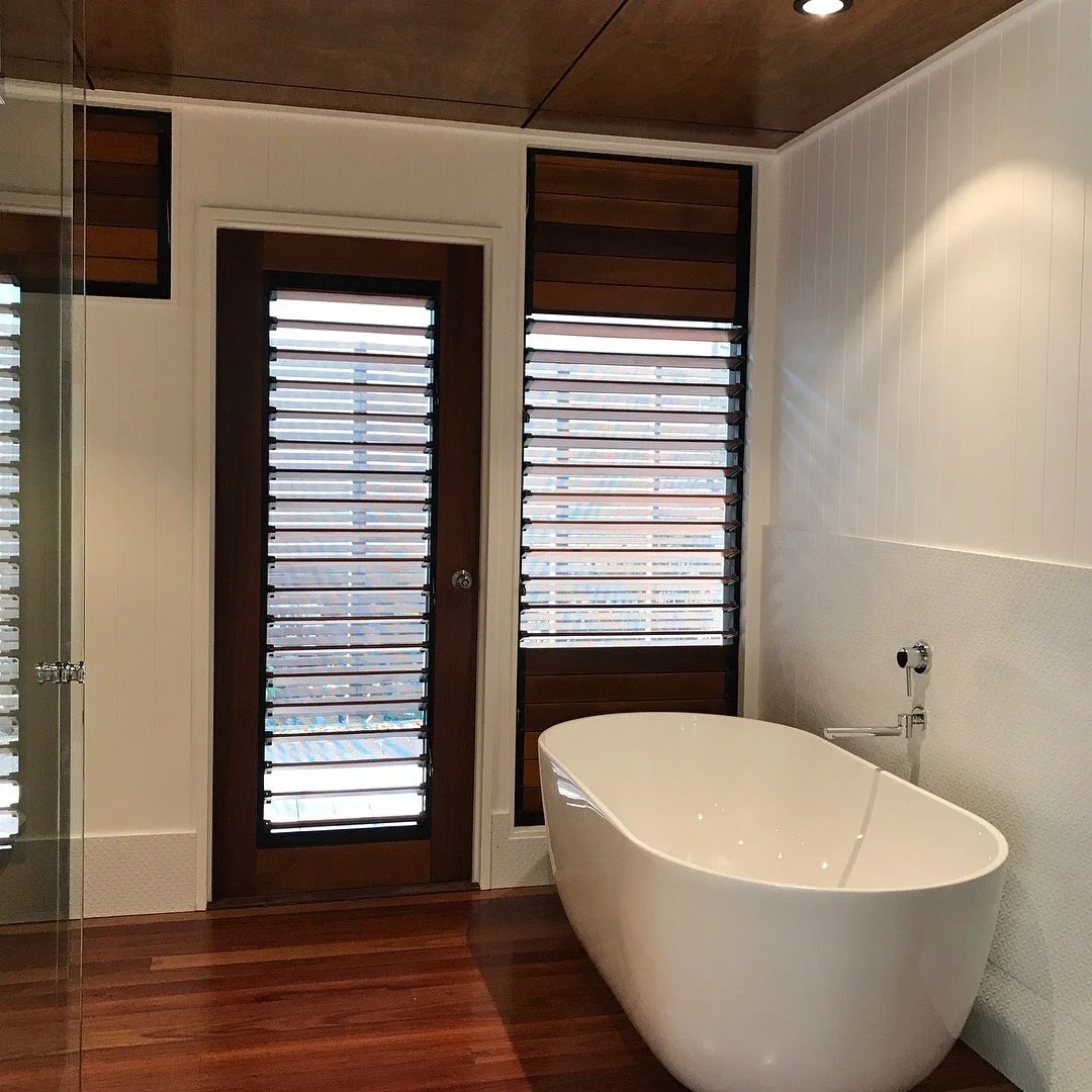 Modern bathroom with a freestanding bathtub, wooden floor, and windows with horizontal adjustable blinds.