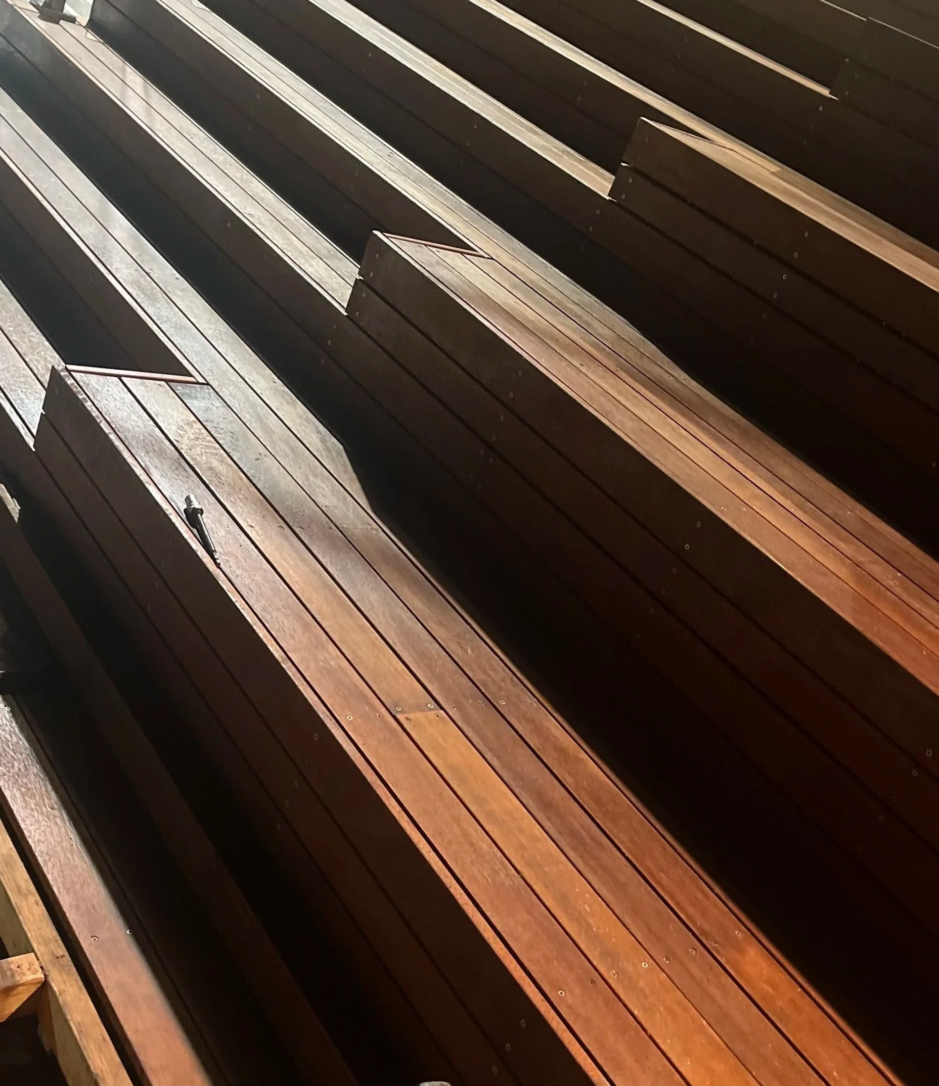 Close-up of a wooden bench with slats and metal armrests, part of a series of benches in an outdoor setting.