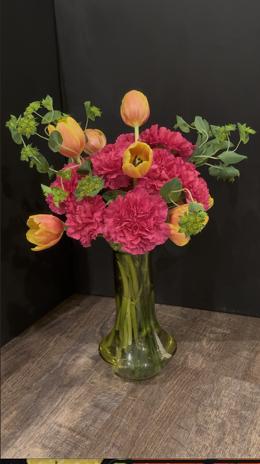 Concierge Desk Statement Arrangement — coral tulips and fuchsia carnations styled in a tall green glass vase for a bold, welcoming entrance moment.