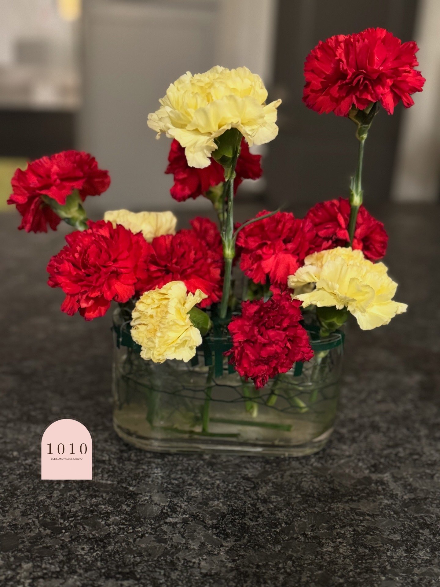 Petite Countertop Accent (Front View) — red and buttercream carnations arranged in a low vessel for host stands, bars, or welcome tables.