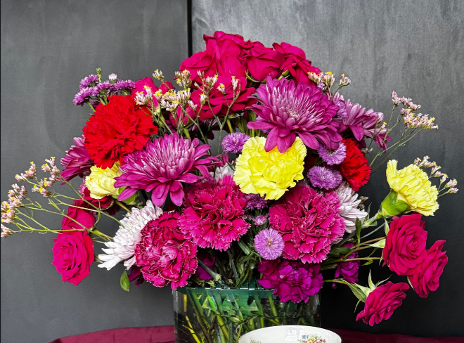 A vibrant bouquet of pink, red, yellow, and purple flowers in a glass vase on a table.