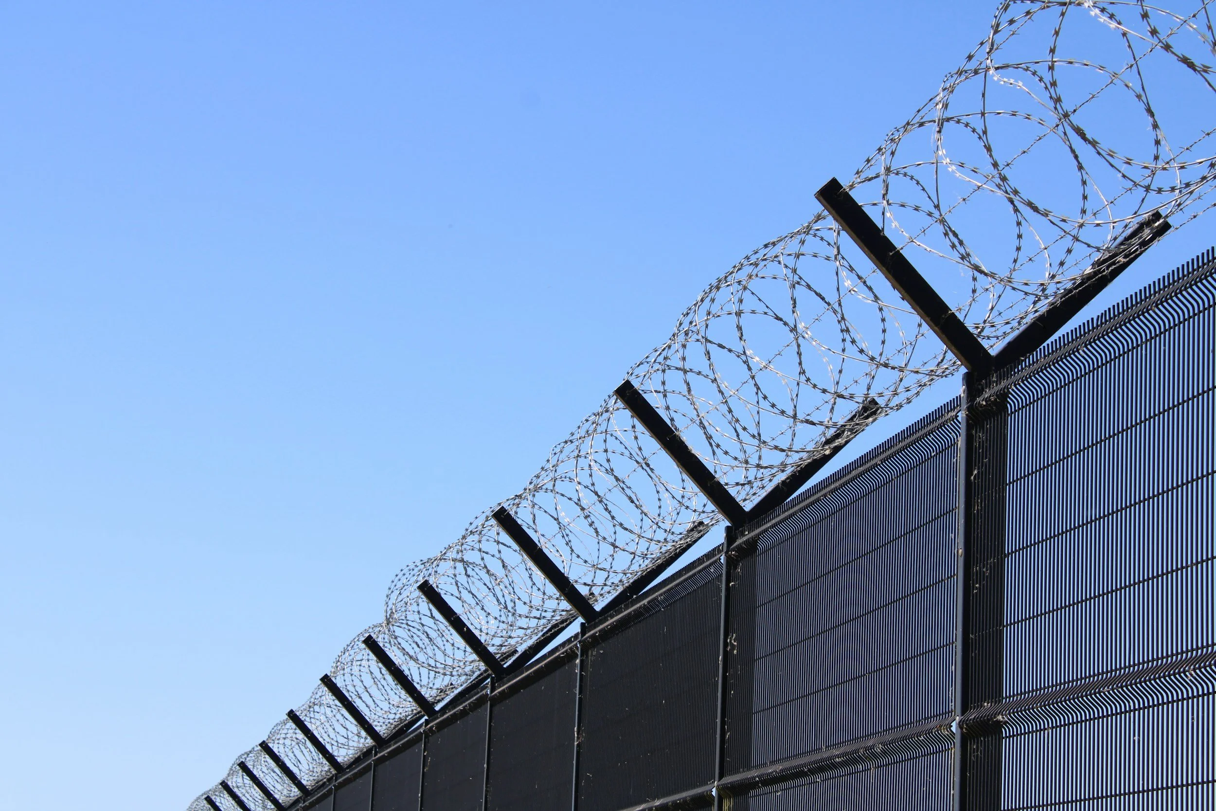 Security fence topped with concertina razor wire against a blue sky.