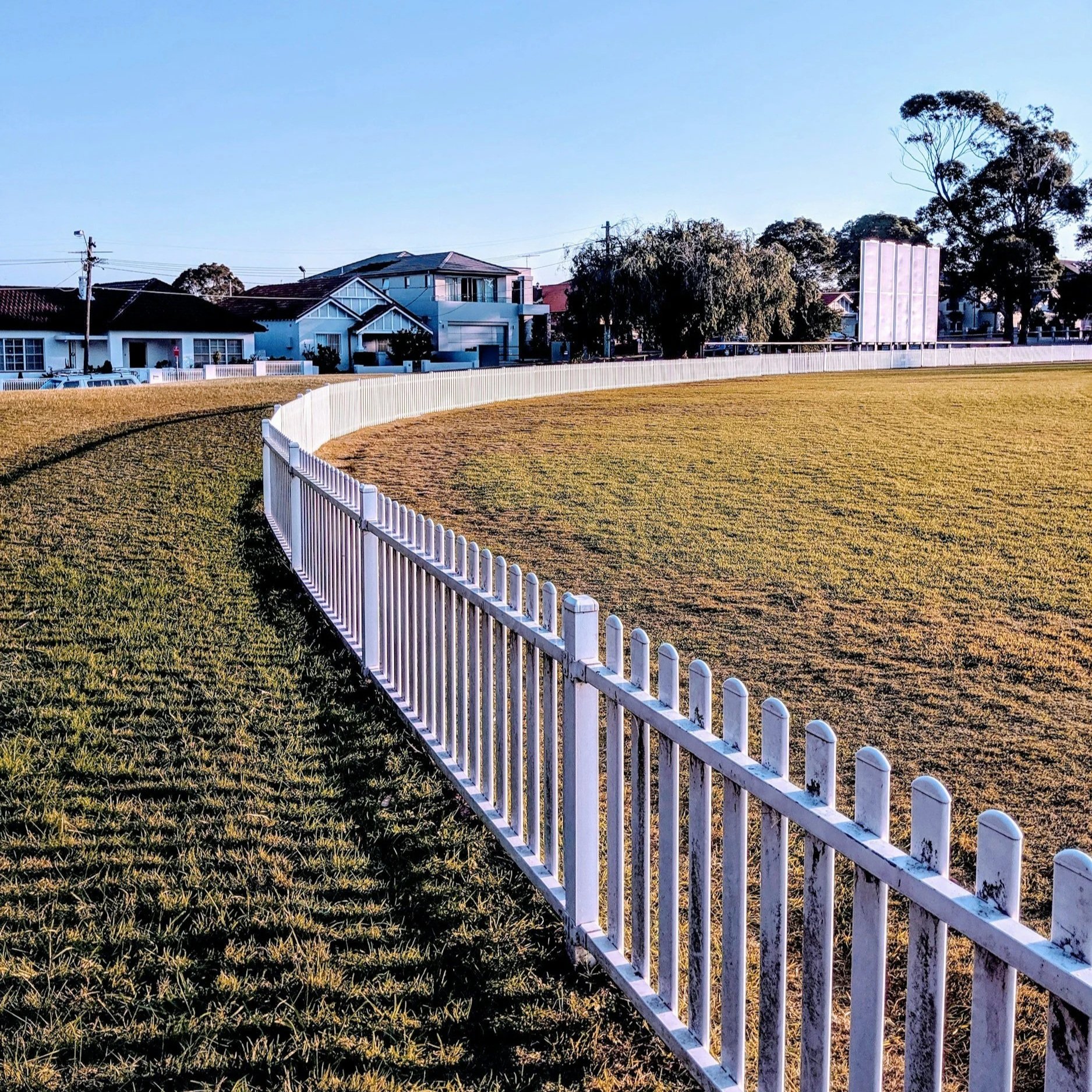 Curved white fence across grassy field, symbolizing maintained boundaries and transition from aging aluminum fencing to stronger, visually appealing fence solutions.