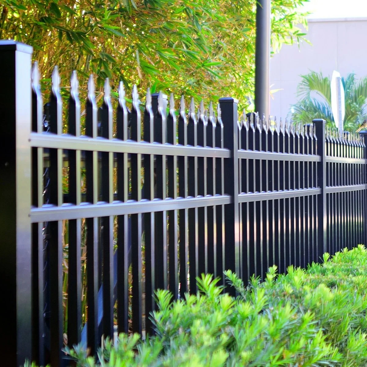 Close view of black metal picket fence with decorative spear tops beside shrubs, illustrating sturdy commercial fencing requiring timely maintenance and repair