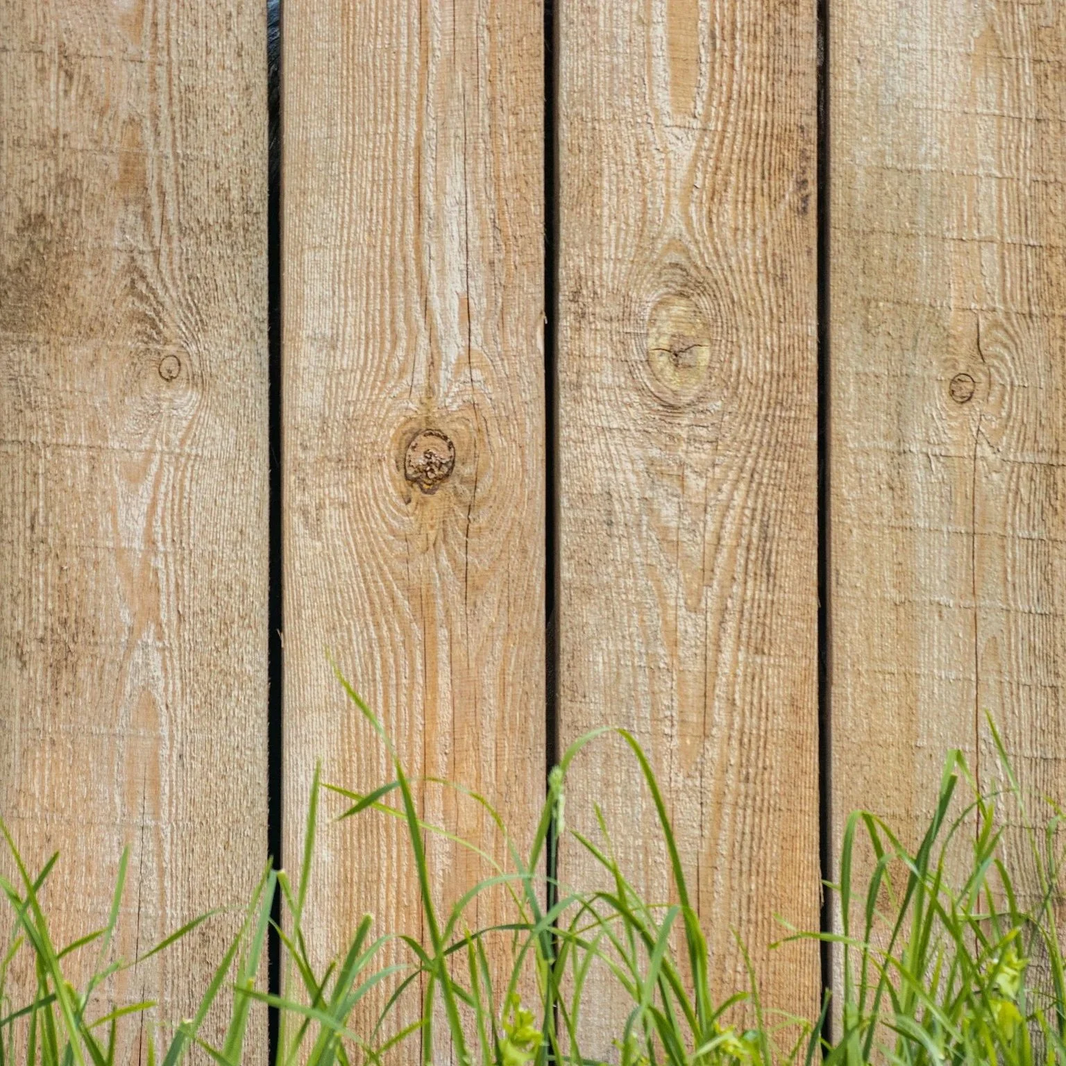 Wooden fence boards with natural finish and grass below, symbolizing cleared space and readiness for new fence installation after professional demolition services.