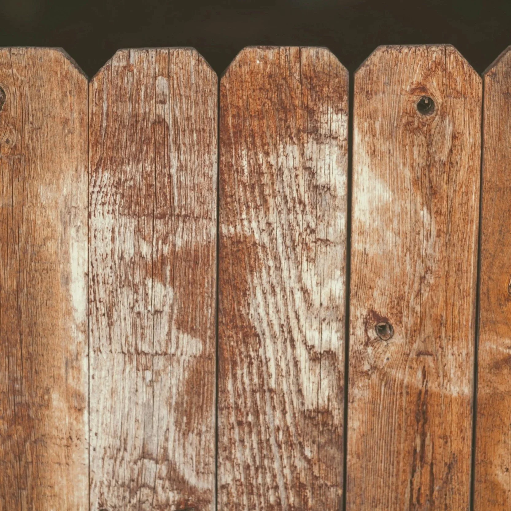 Close-up of worn wooden fence boards with visible aging, representing need for strong, long-lasting fencing materials in active sports facility installations.