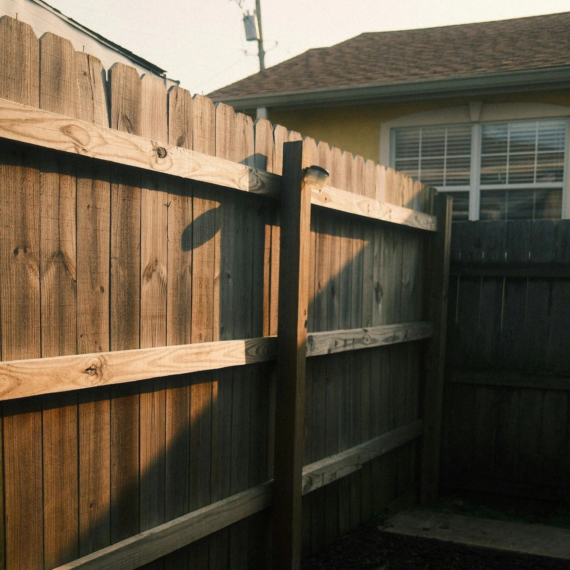 Old wooden backyard fence showing weather damage and structural wear, illustrating warning signs requiring fence replacement instead of repairs.