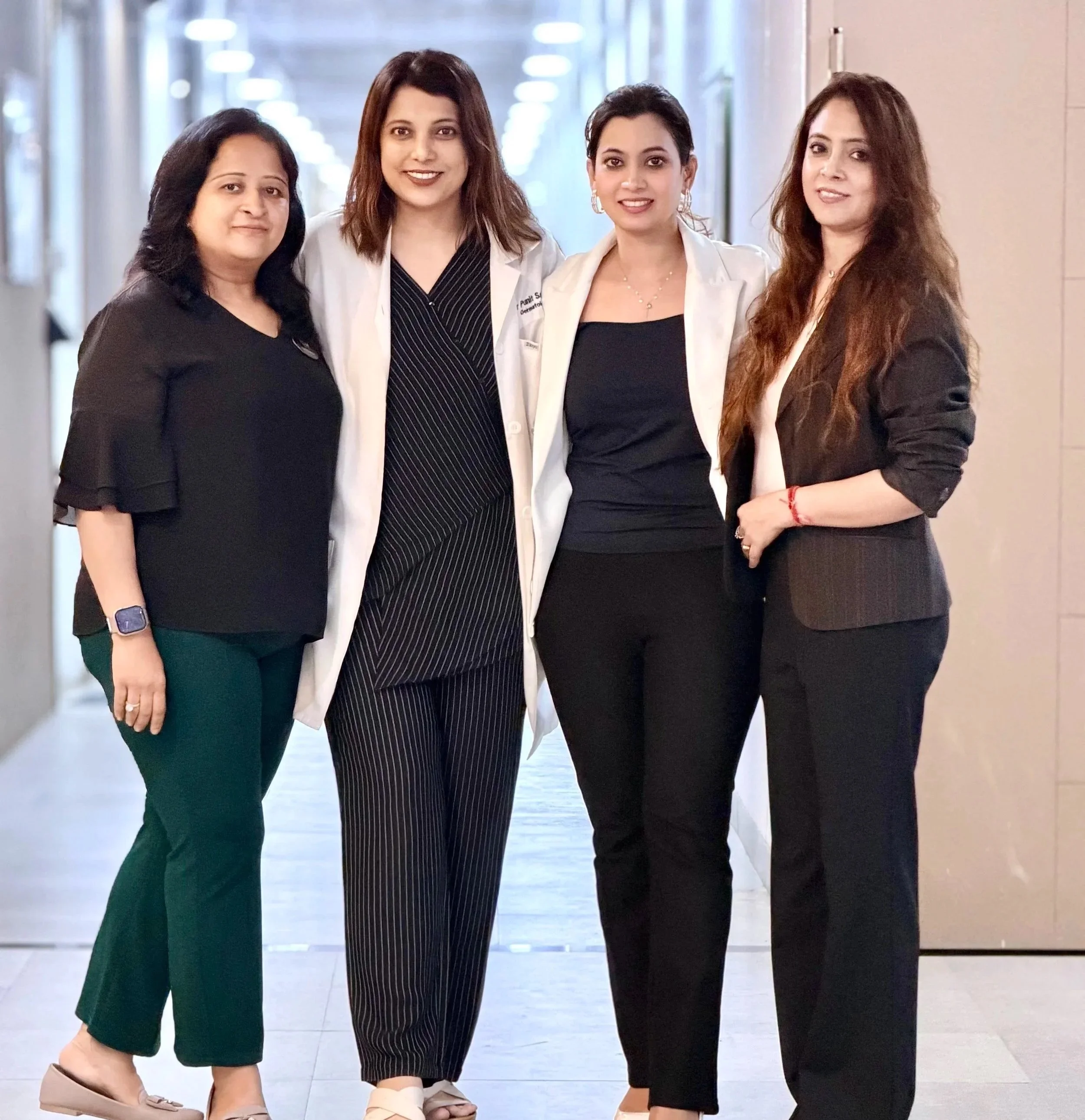 Four women standing in a hallway, posing for a photo, with three women in professional attire and one in casual attire.