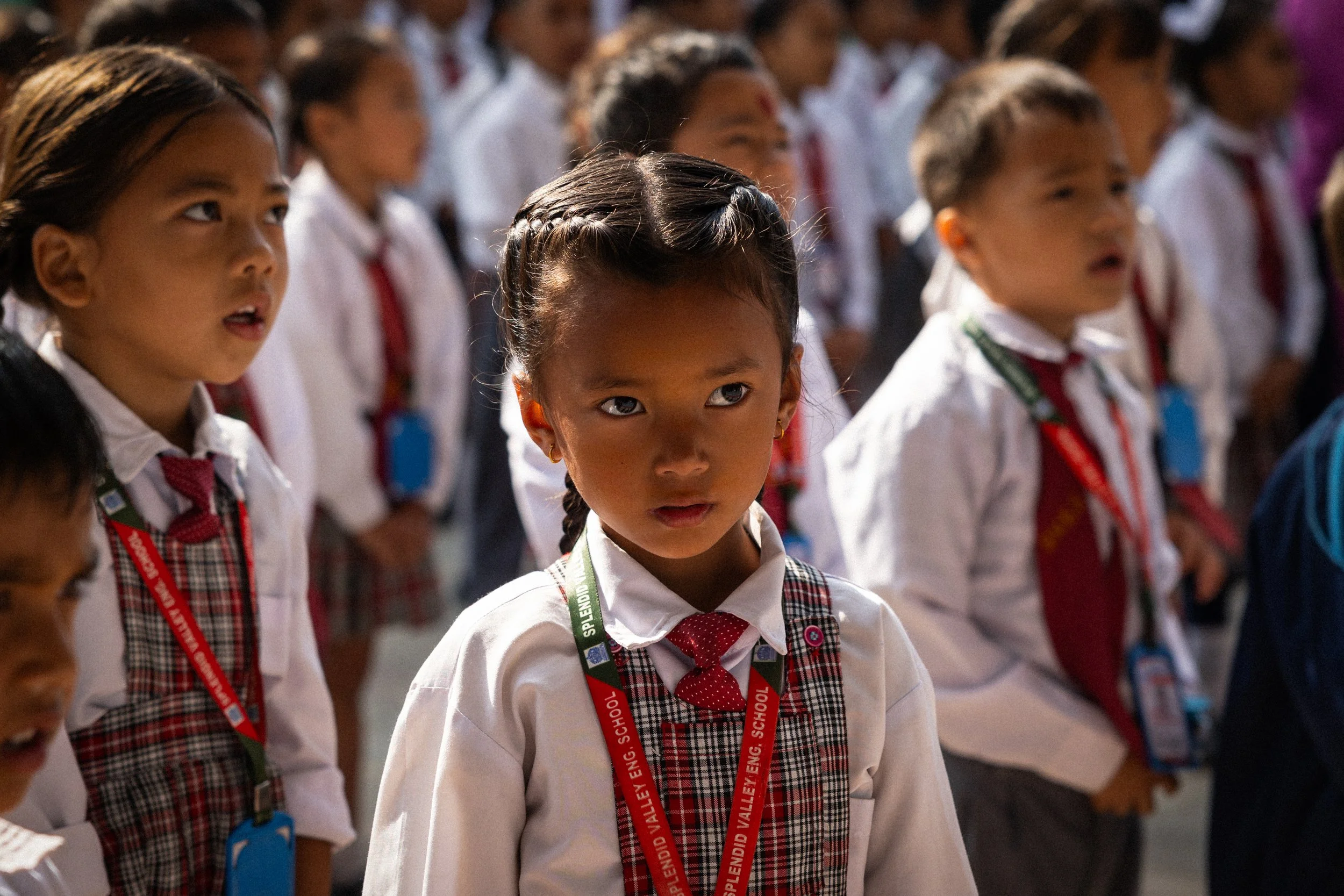 Ragazze scolarette in divisa, alcune cantano, una in primo piano guarda seriamente.
