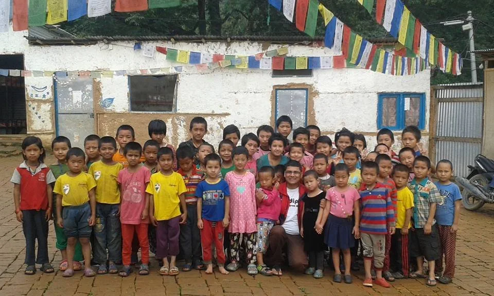 Gruppo di bambini e adulti davanti a una casa con bandiere colorate appese sopra