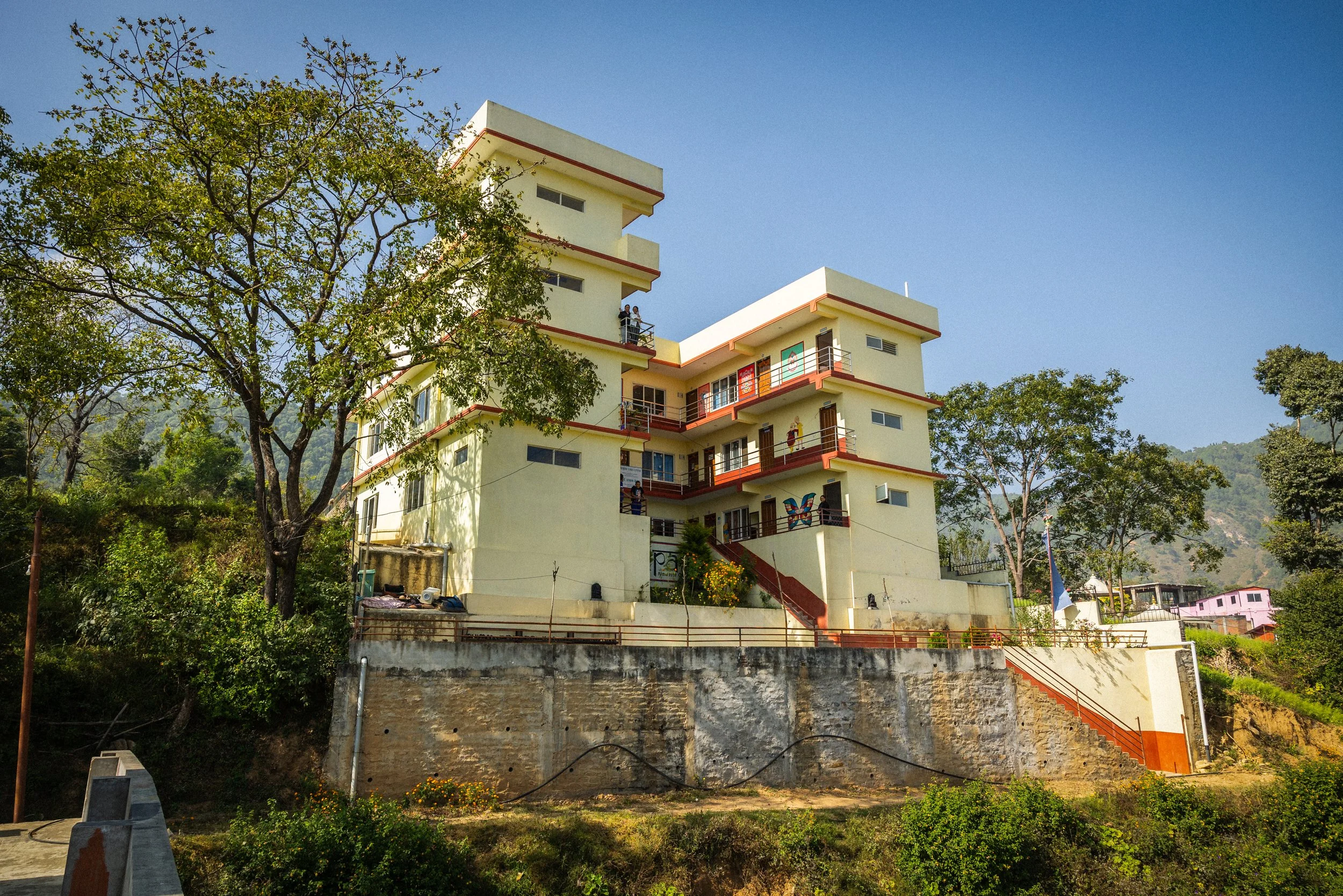 Edificio multicolore in stile moderno su una collina circondato da alberi e vegetazione, con un cielo limpido