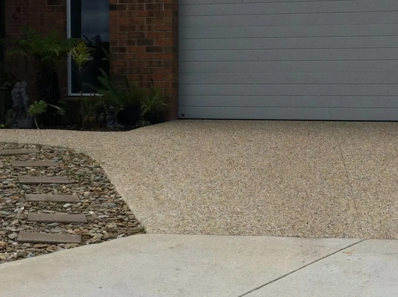 View of a garage door with concrete driveway and landscaped area with rocks and plants.
