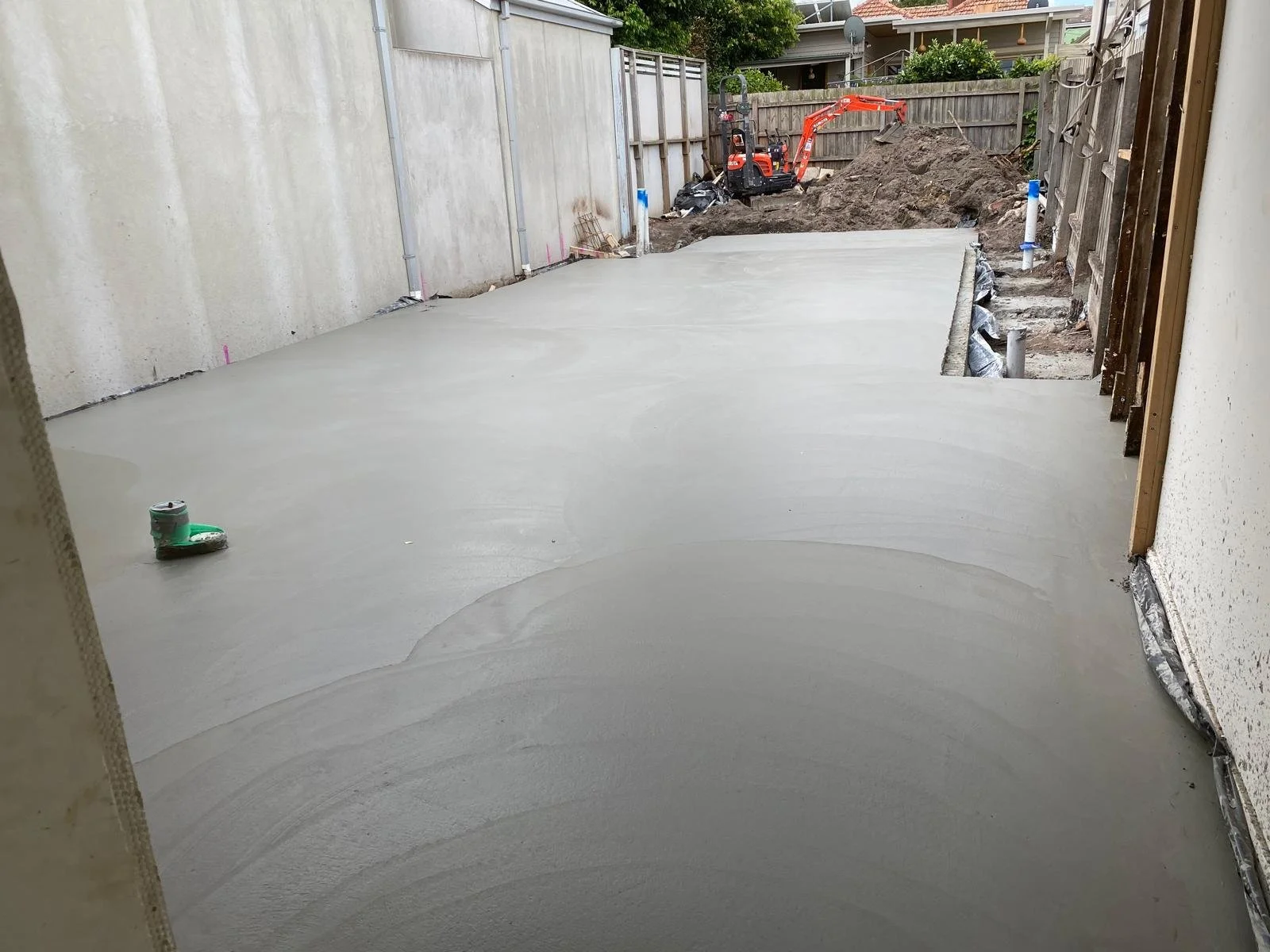 Freshly poured concrete slab at a construction site with construction equipment and dirt pile in the background.