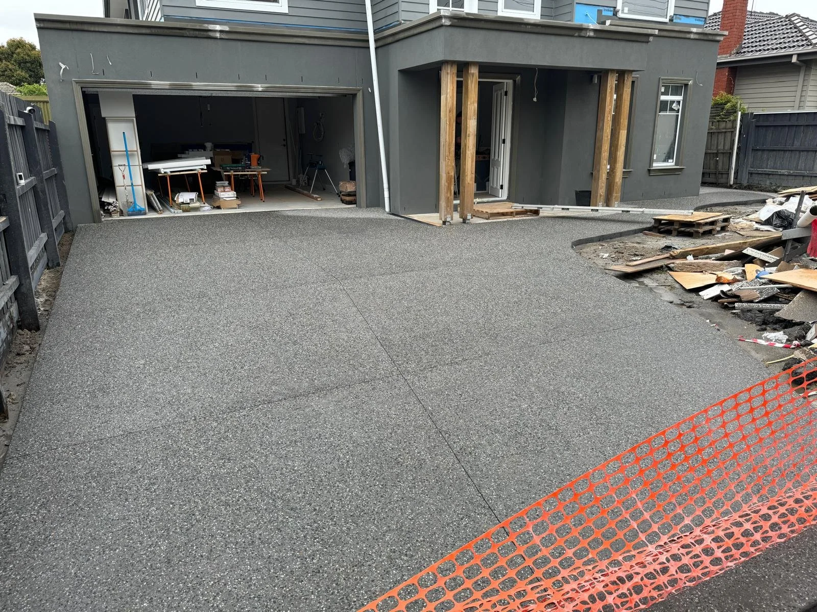 Backyard driveway under construction with fresh new concrete, construction materials, and tools visible in the background.
