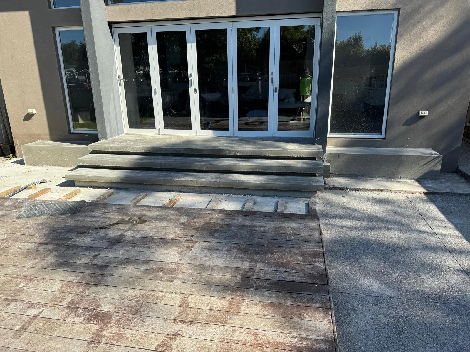 Construction site with a building entrance featuring stairs, glass doors, and a wooden and concrete deck surface.