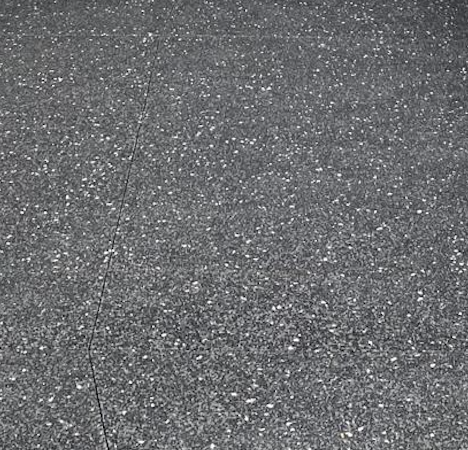 Close-up of a gray asphalt pavement with a crack running diagonally.