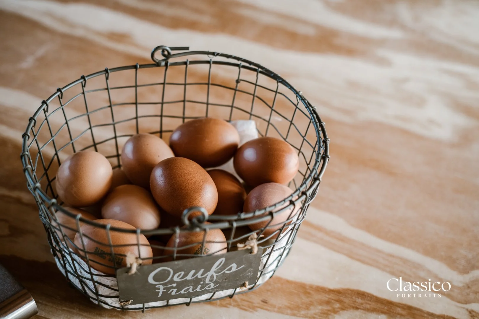 A wire basket filled with brown eggs on a wooden surface.