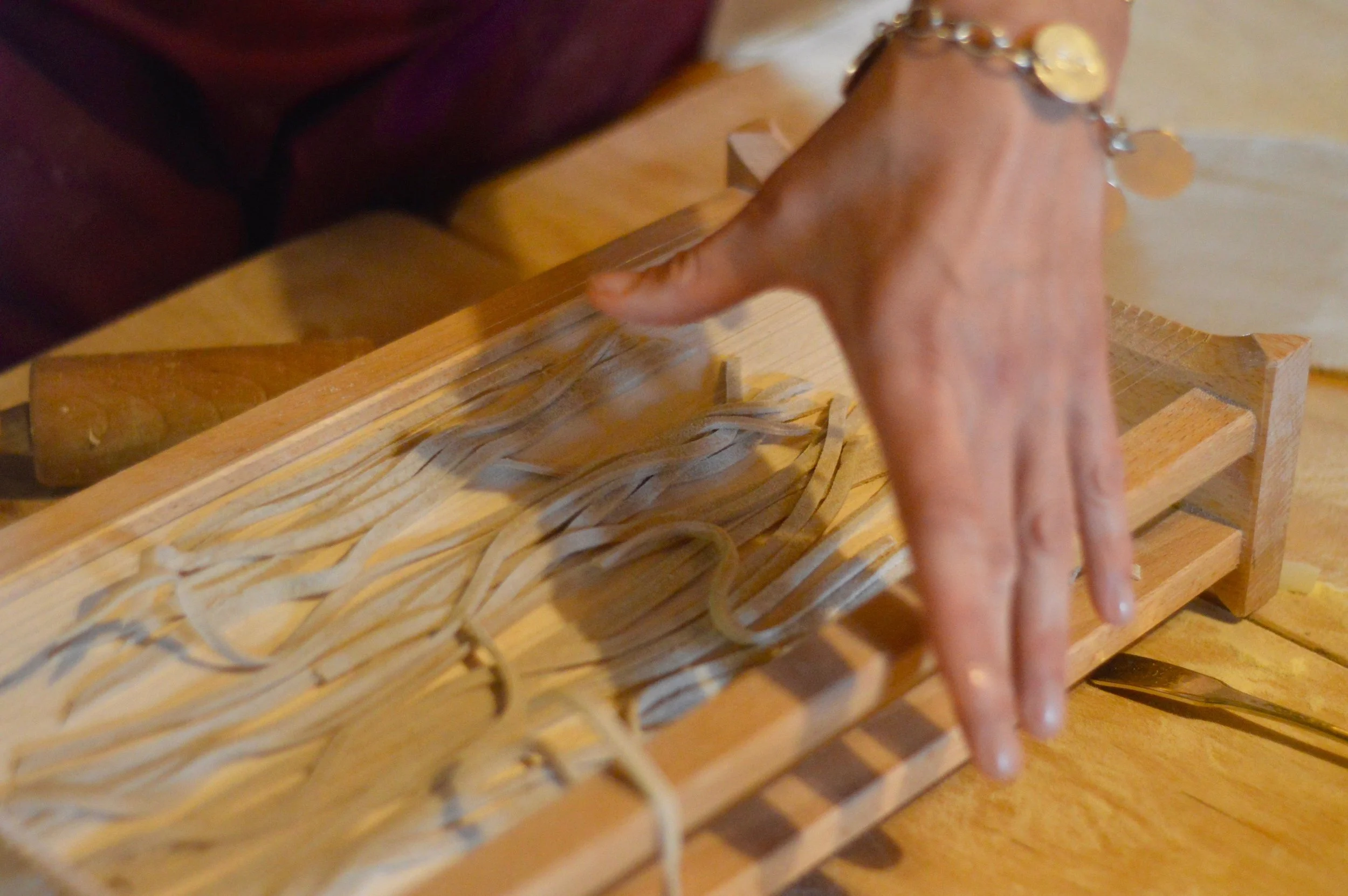 Close-up of a person's hand using a wooden pasta machine to roll fresh pasta dough into thin sheets.