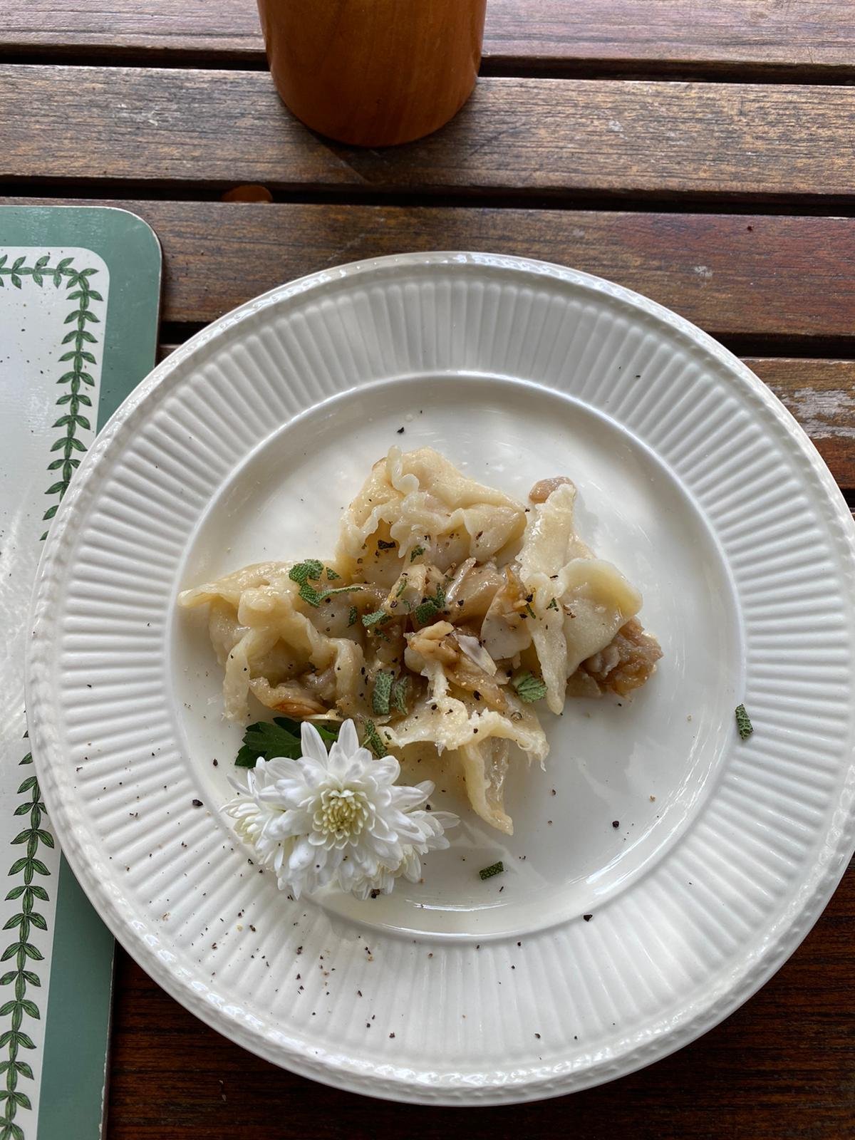 Plate of cooked ravioli garnished with herbs and a white flower, on a wooden table.