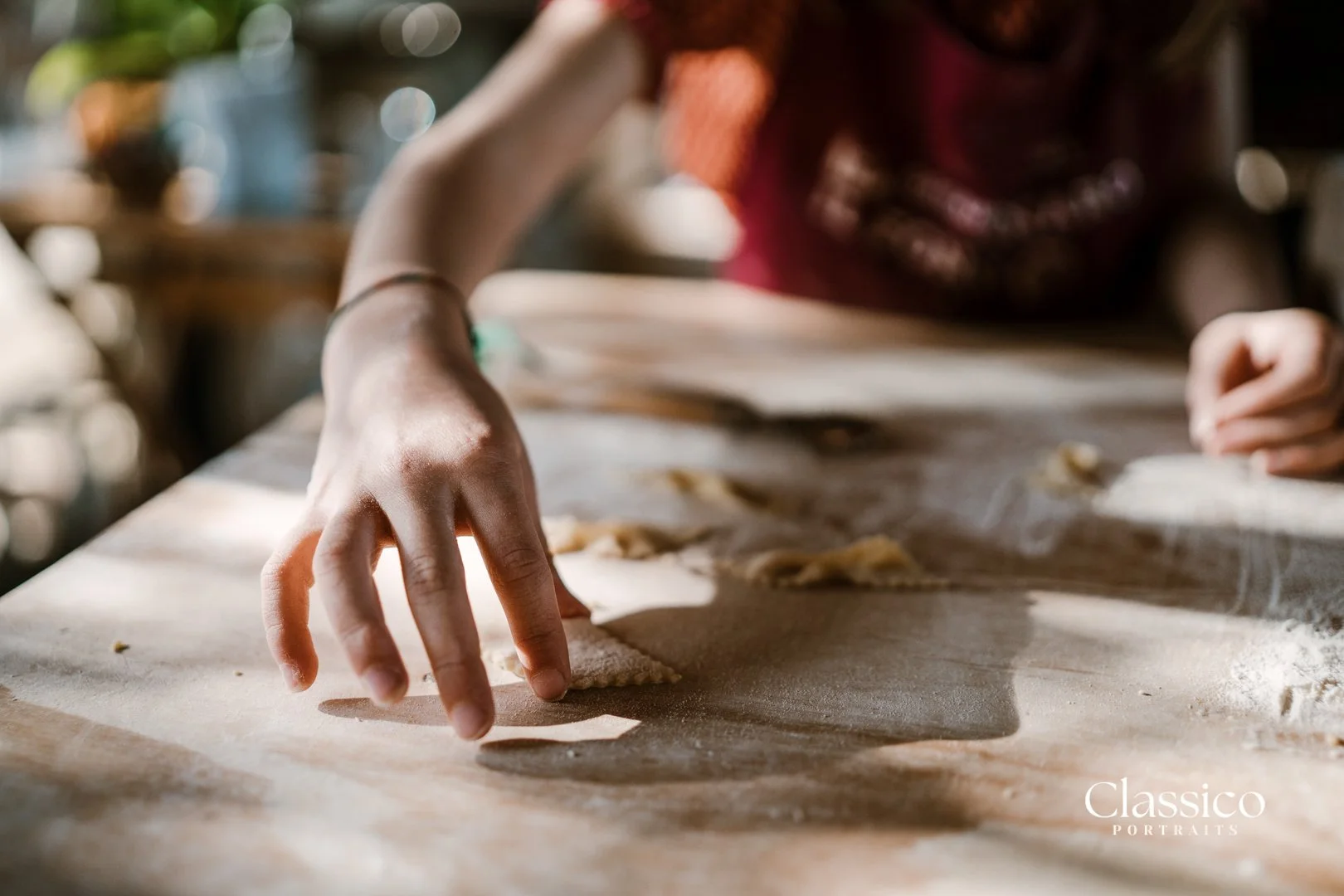 Close-up of a person's hand shaping dough on a floured surface, with a blurred background.