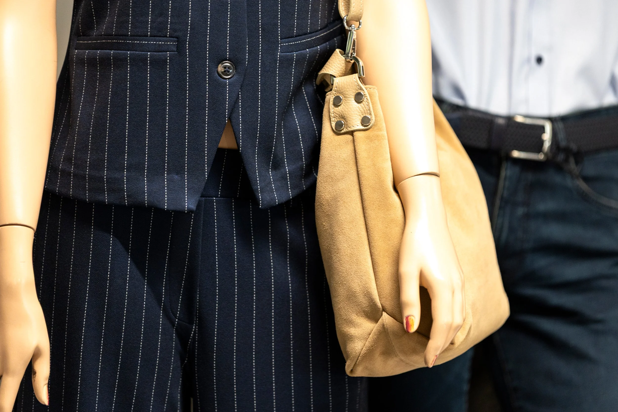 Nahaufnahme eines eleganten schwarzen Anzugs mit weißen Längsstreifen, dazu beige Handtasche und die Hand eines Modells mit Fingernägeln mit rotem und gelbem Muster.