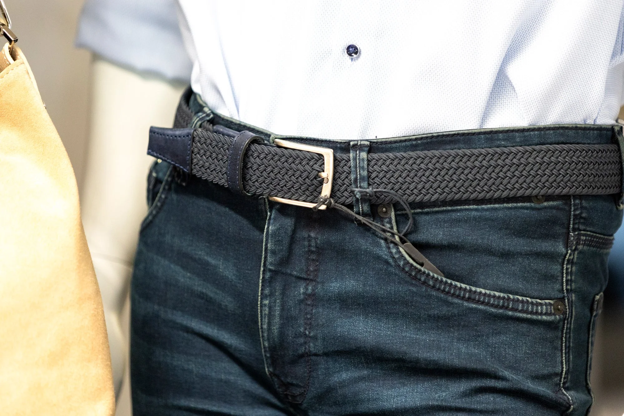 Nahaufnahme eines Mannes, der eine weiße Hemd trägt und eine schwarze, geflochtene Ledergürtel um die Taille trägt. Neben ihm befindet sich eine Person mit einem gelben Kleidungsstück.
