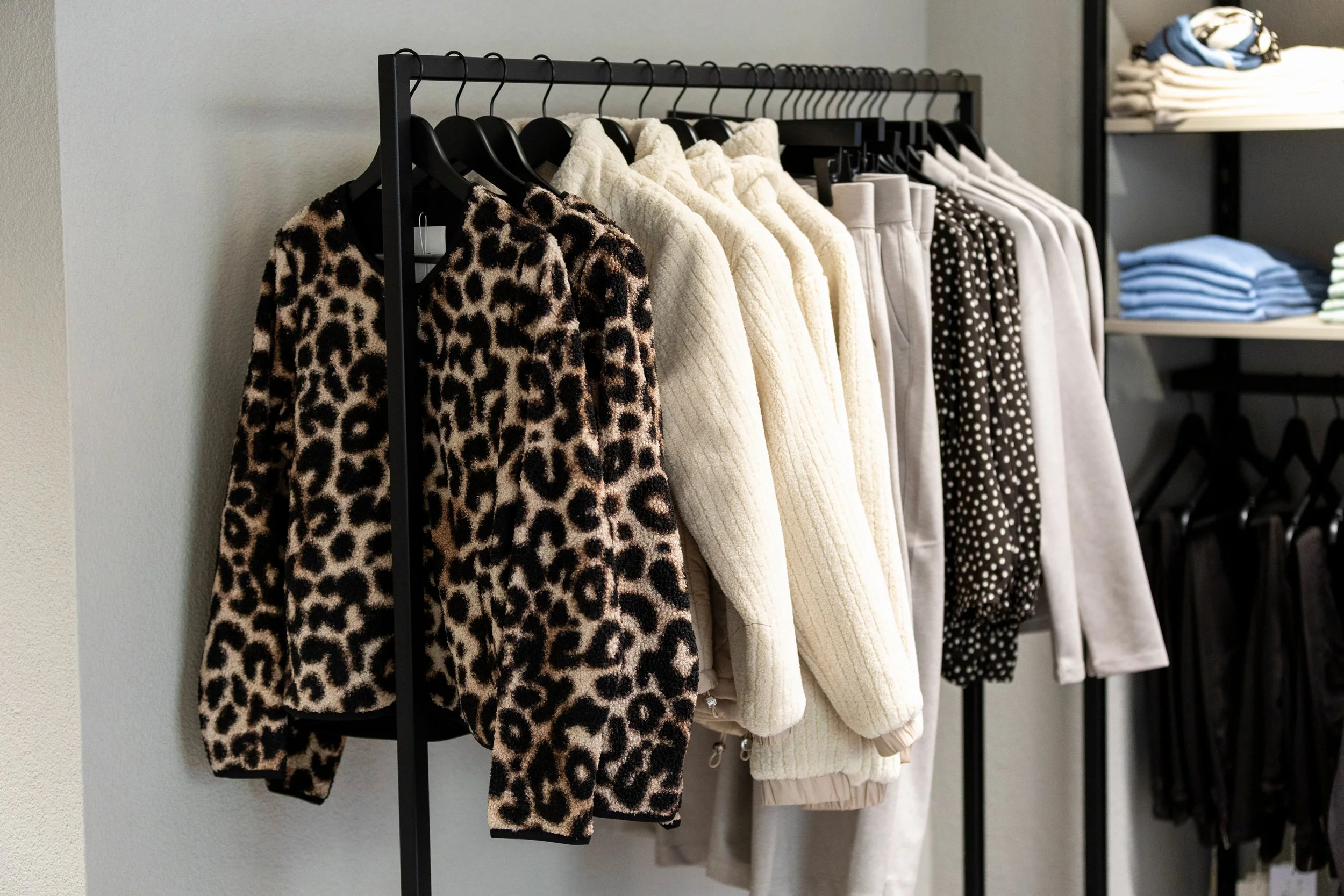 Kleiderständer mit Fellmuster-Pullover, weißen Pullover, gepunktetem Kleid und weiteren Kleidungsstücken