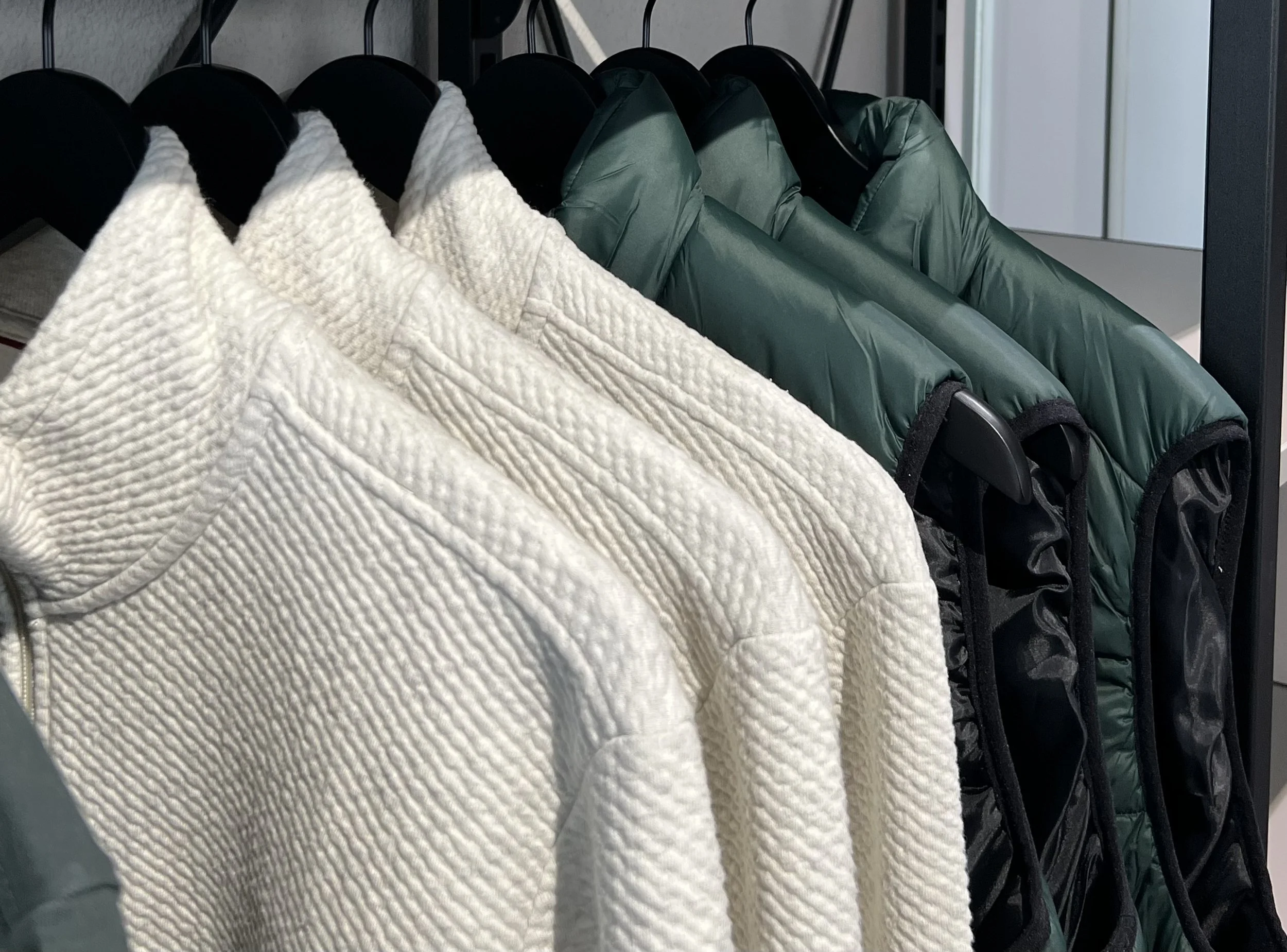 Herrenjacken in Weiß und Grün hängen an Garderobenstangen in einem Kleiderschrank.