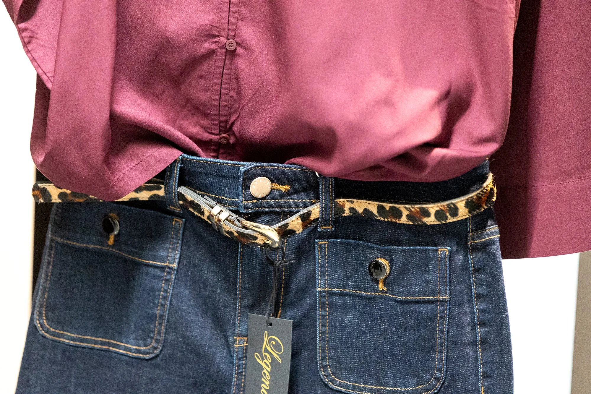 Einoberkörper eines Menschen trägt eine rosa Bluse, eine Leoband-Hüftschürze und eine dunkle Denim-Jeans.